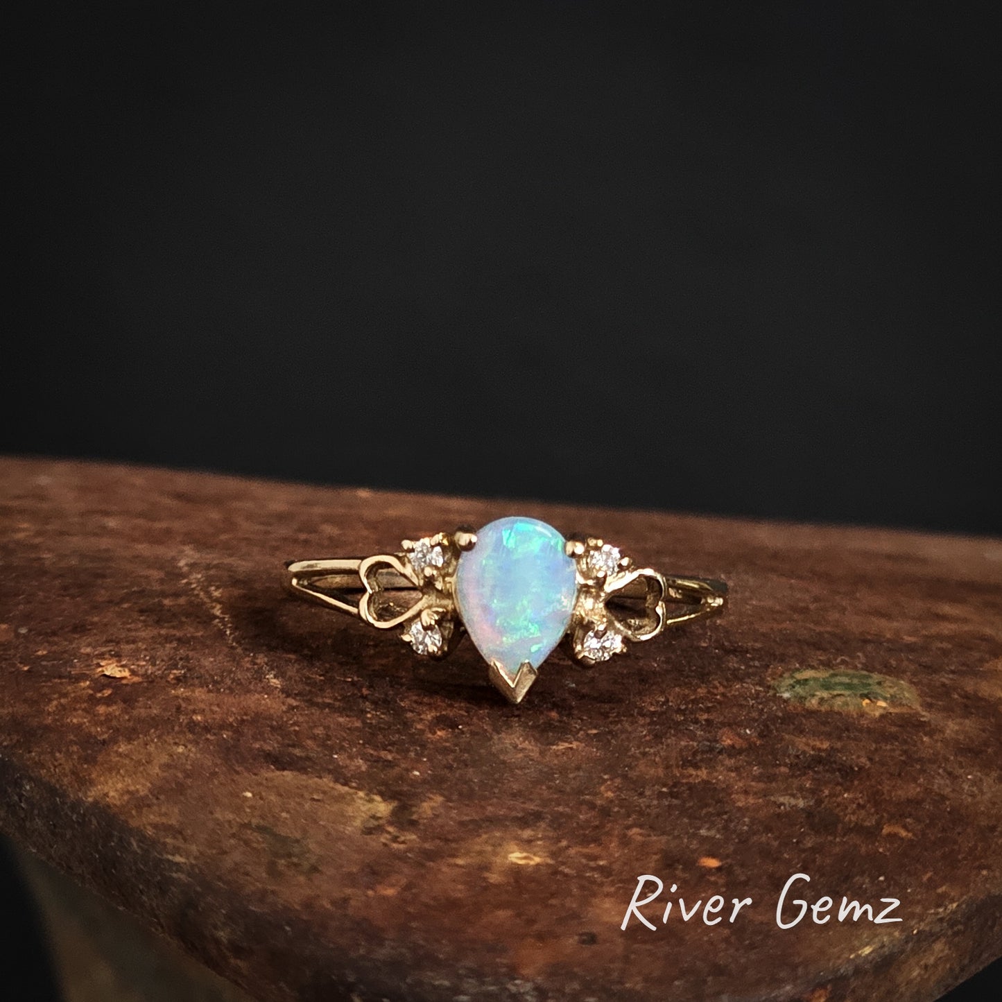 Green swirls on a blue base shown in the crystal opal set in yellow gold ring.