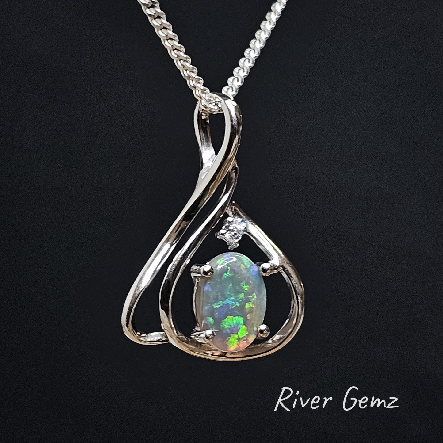 Oval shaped opal with green, blue and orange spheres of colour claw set in modern design silver pendant.