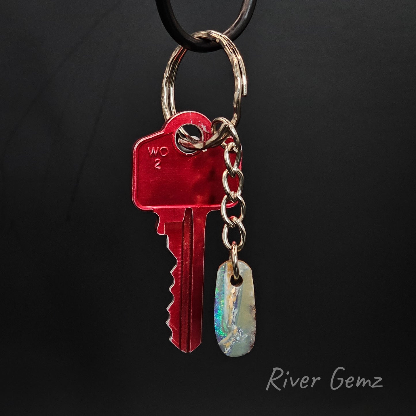 A small boulder opal on a key chain with a red key on a black background, branded 'River Gemz'.