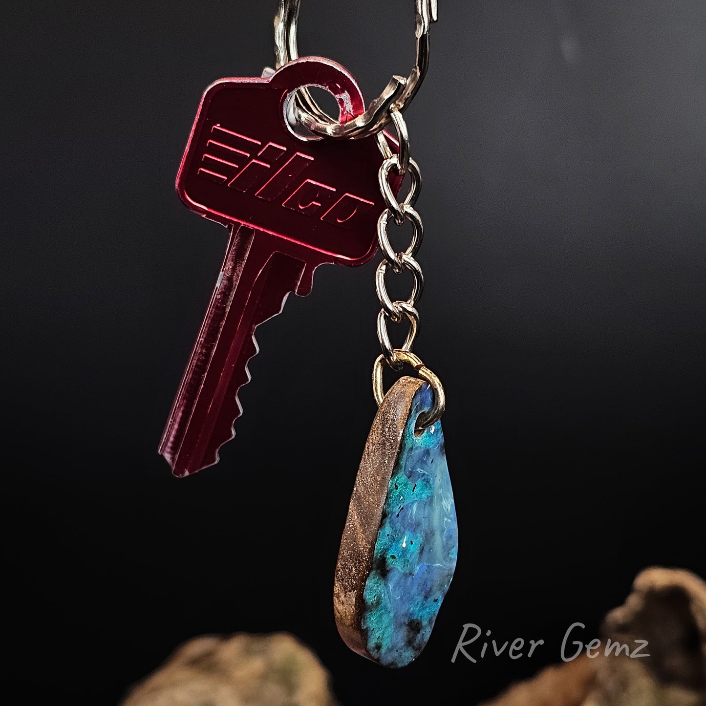 Keychain with a red key and blue/green boulder opal on a dark background