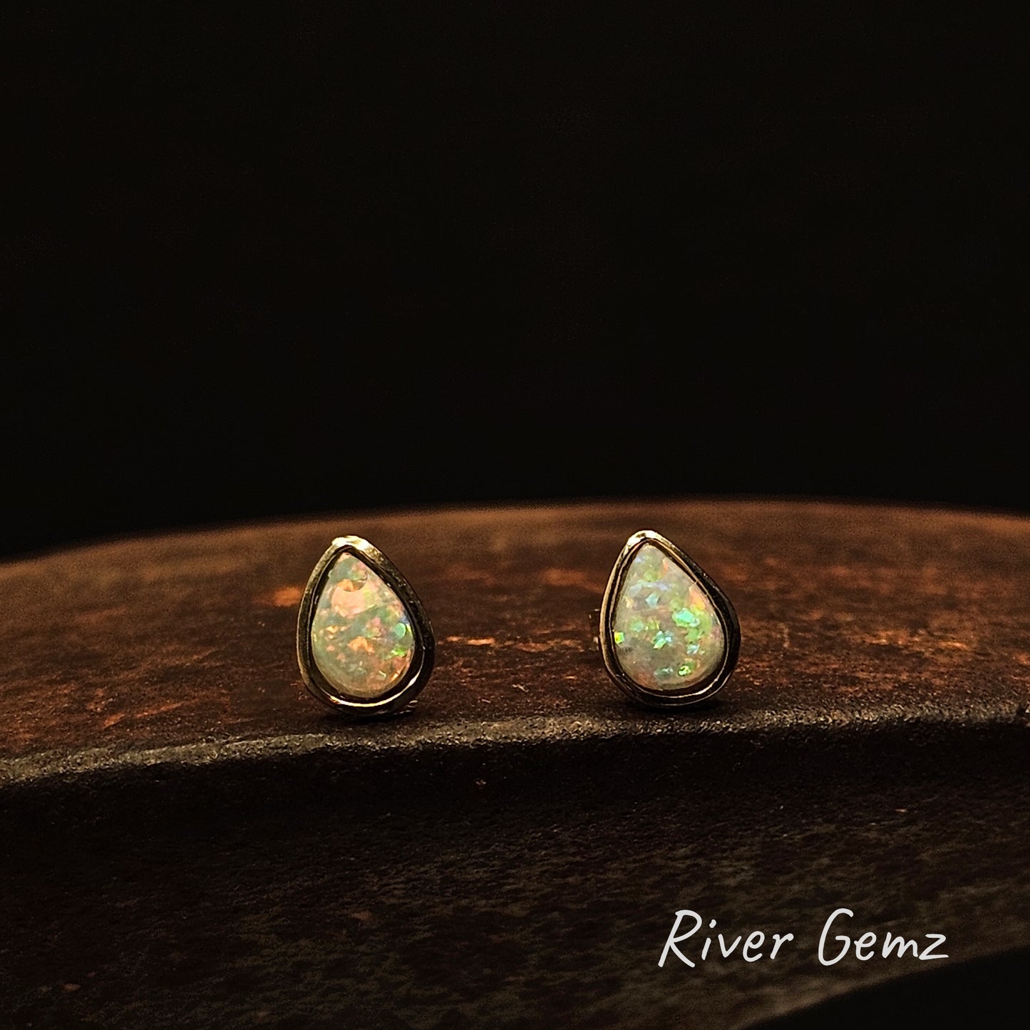 Colourful crystal opals besel set in yellow gold earrings on a cast iron shoe anvil with 'River Gemz' branding.