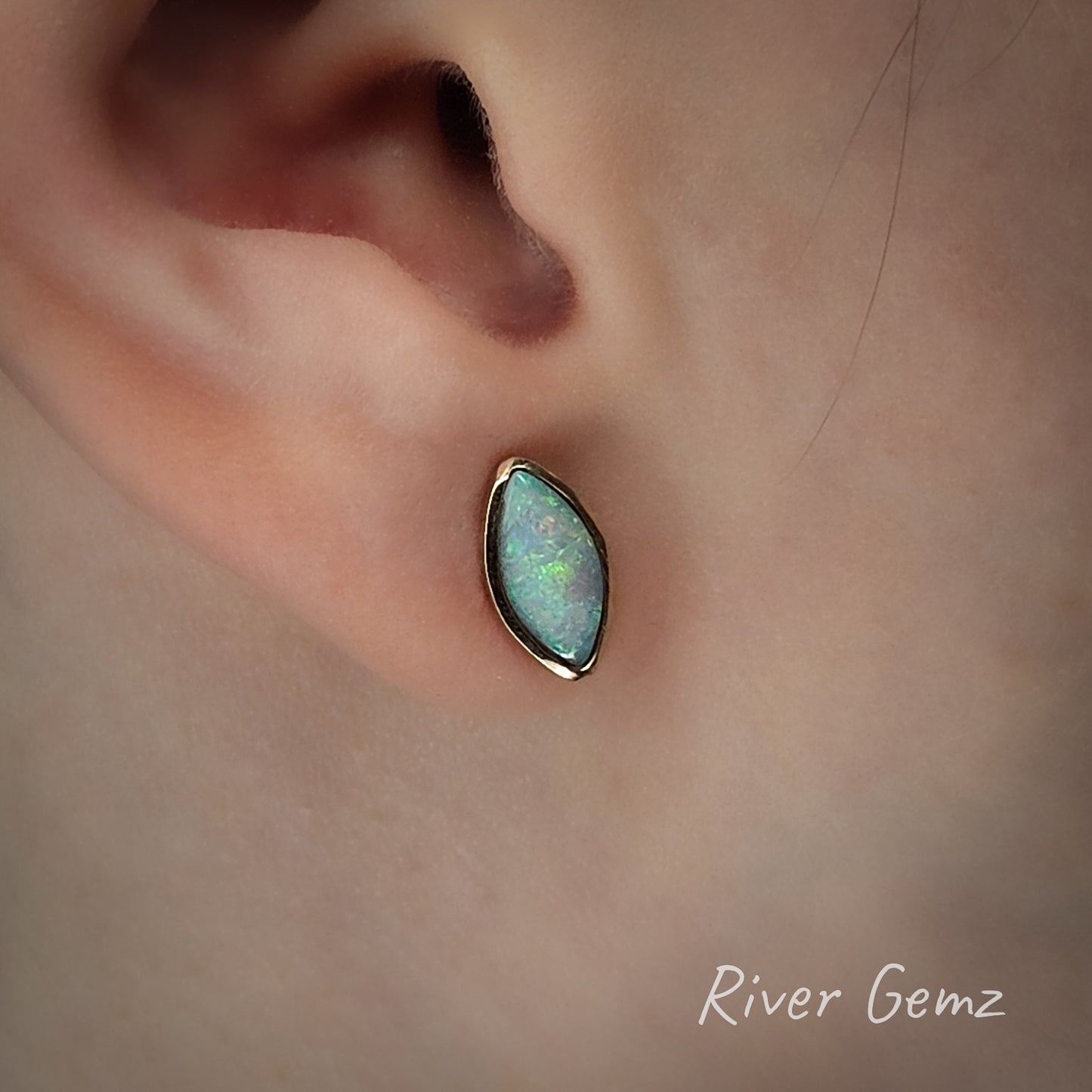 Opal set in gold earring worn on an ear with 'River Gemz' branding.