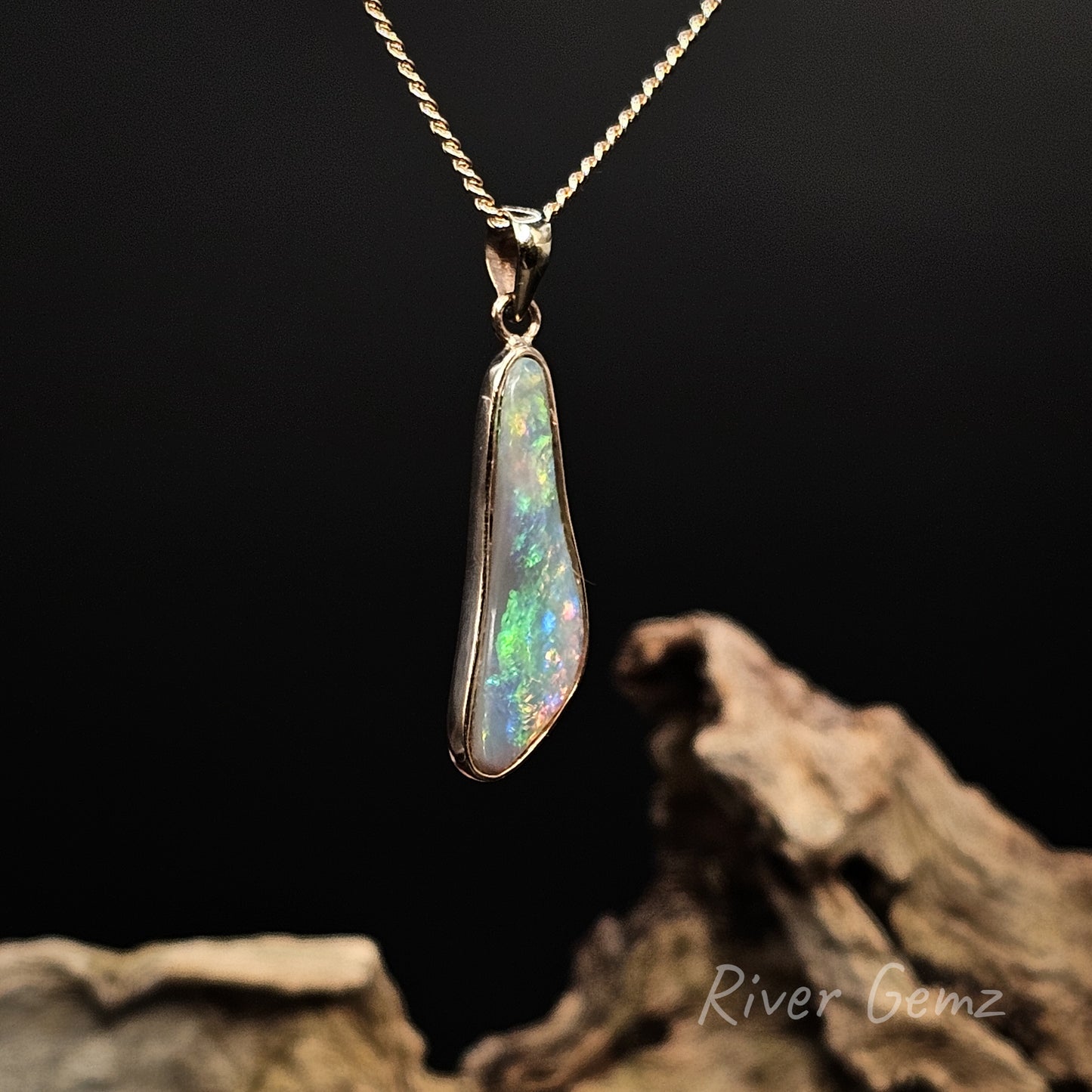 Free form cut opal set in yellow gold pendant on a dark background with 'River Gemz' branding.