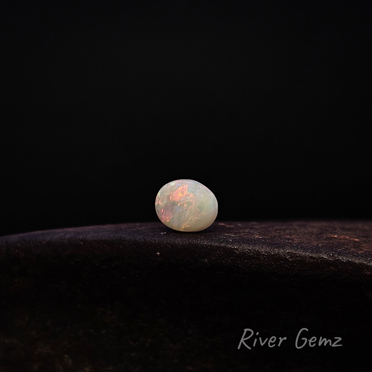 Oval shaped white opal shown in a horizontal position on a dark brown surface and a black background.