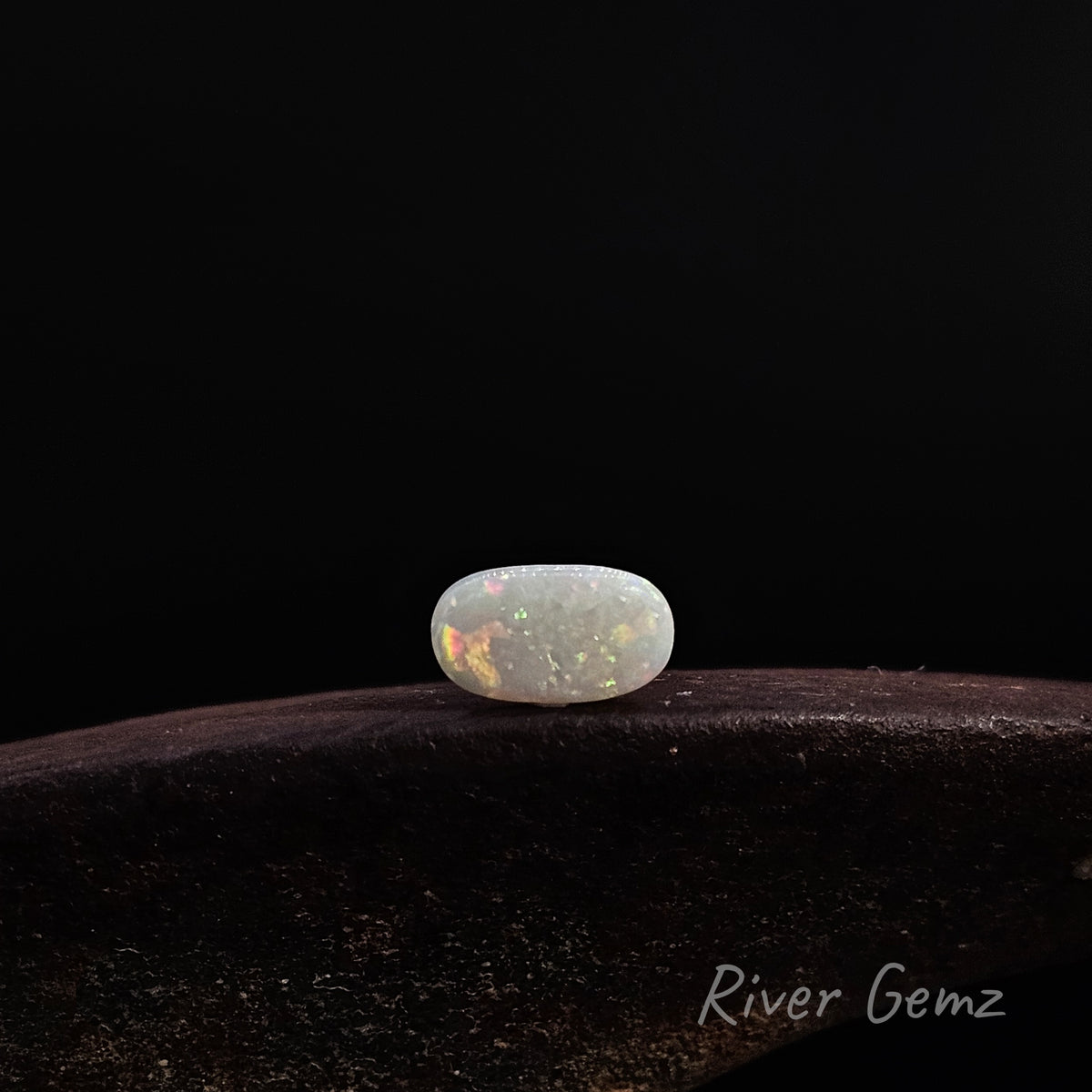 Oval shaped opal show lying horizontally on a brown surface.