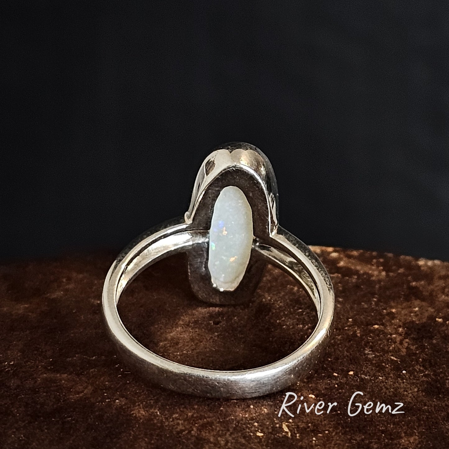 Rear of silver ring showing the white base of the light opal set in it on a dark background, branded 'River Gemz'.