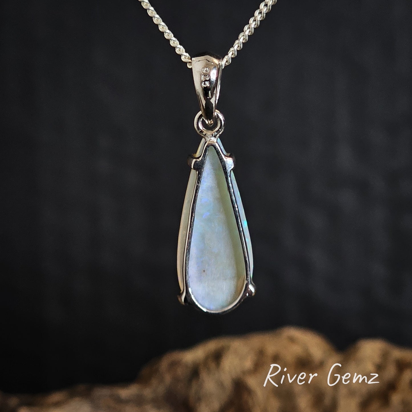 Rear view of the teardrop-shaped pendant with silver frame on a chain against a dark background, featuring 'River Gemz' branding.