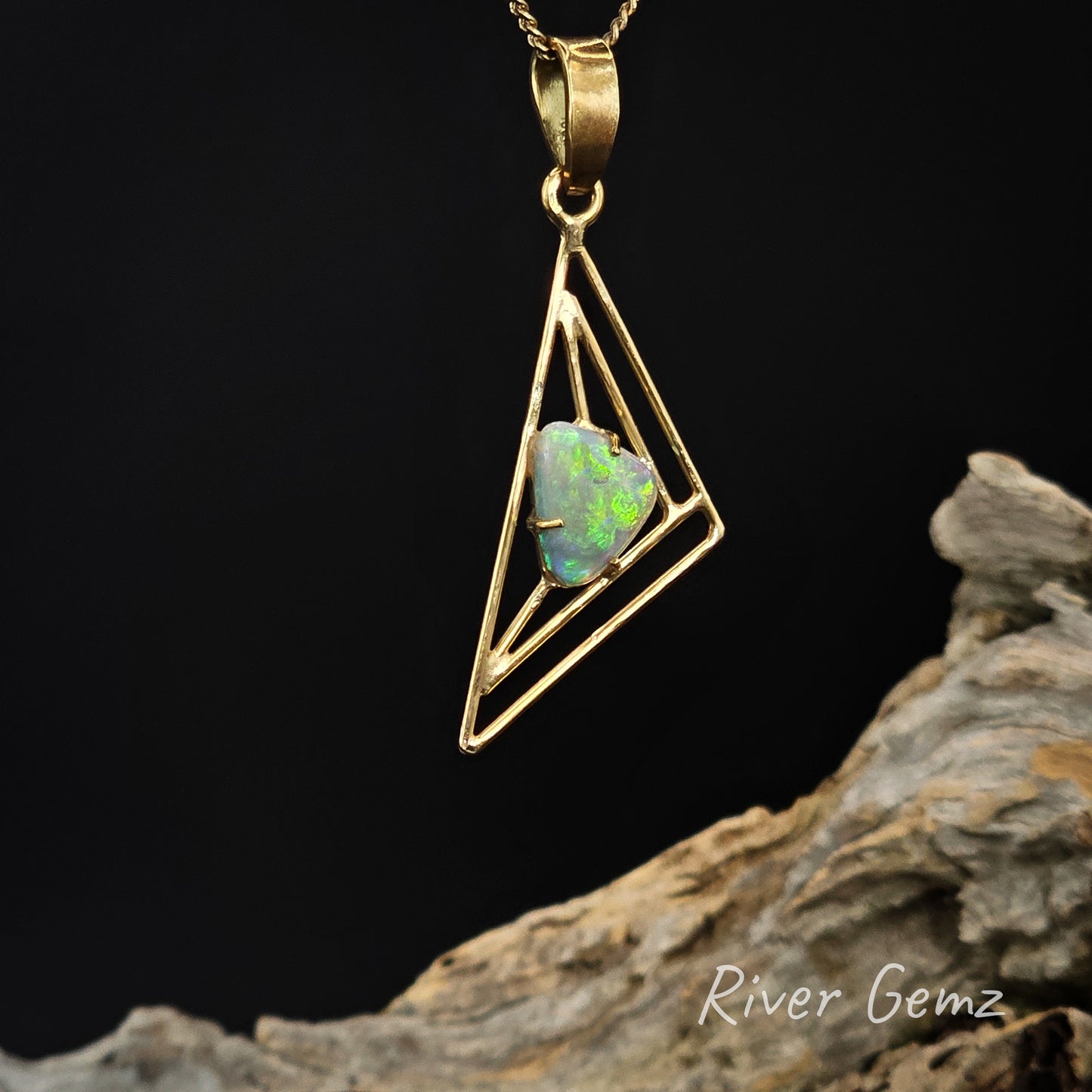 Gold pendant with a triangular design and opal stone on a dark background, featuring 'River Gemz' branding.