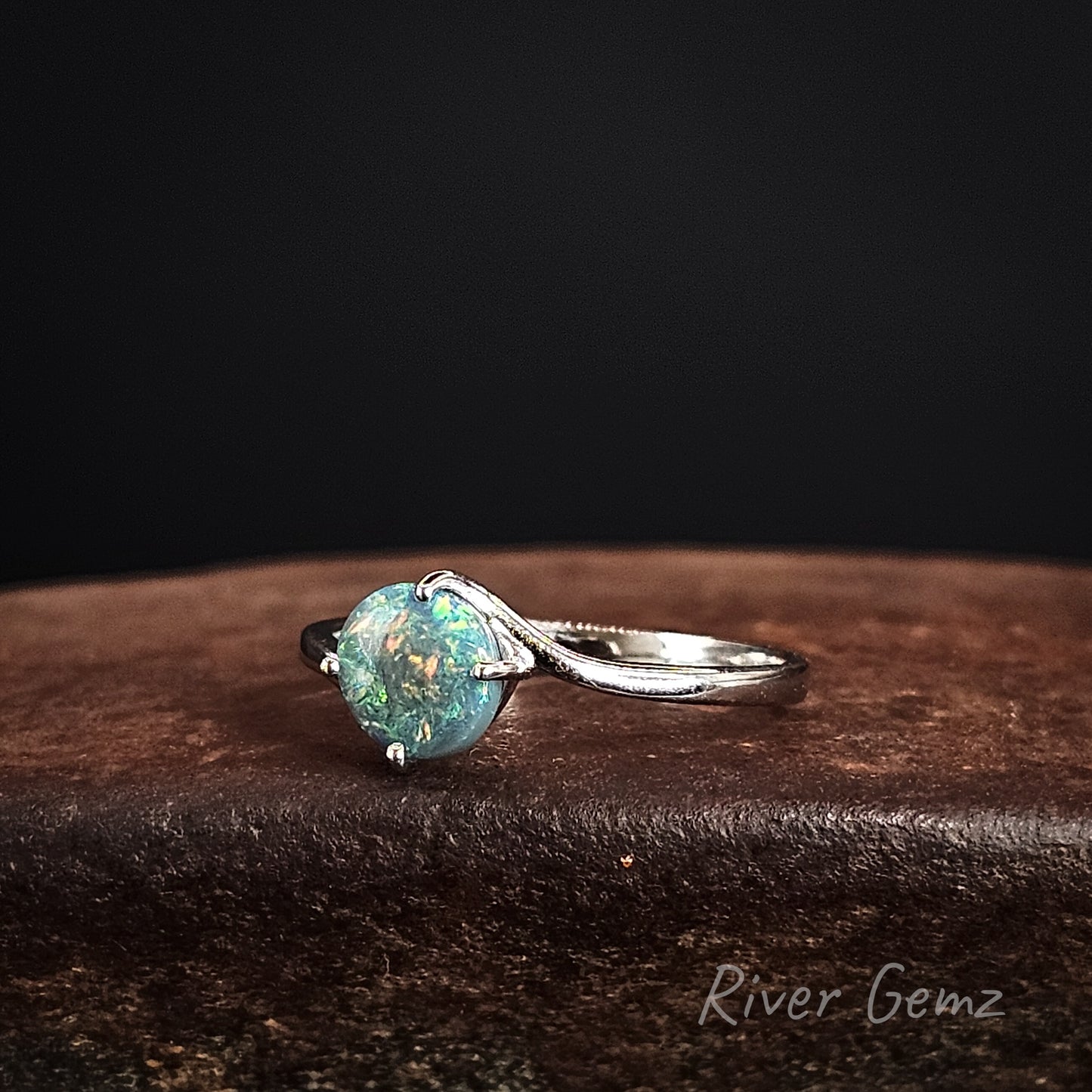 Ring with a multi-coloured round dark opal on a dark background, featuring 'River Gemz' branding.