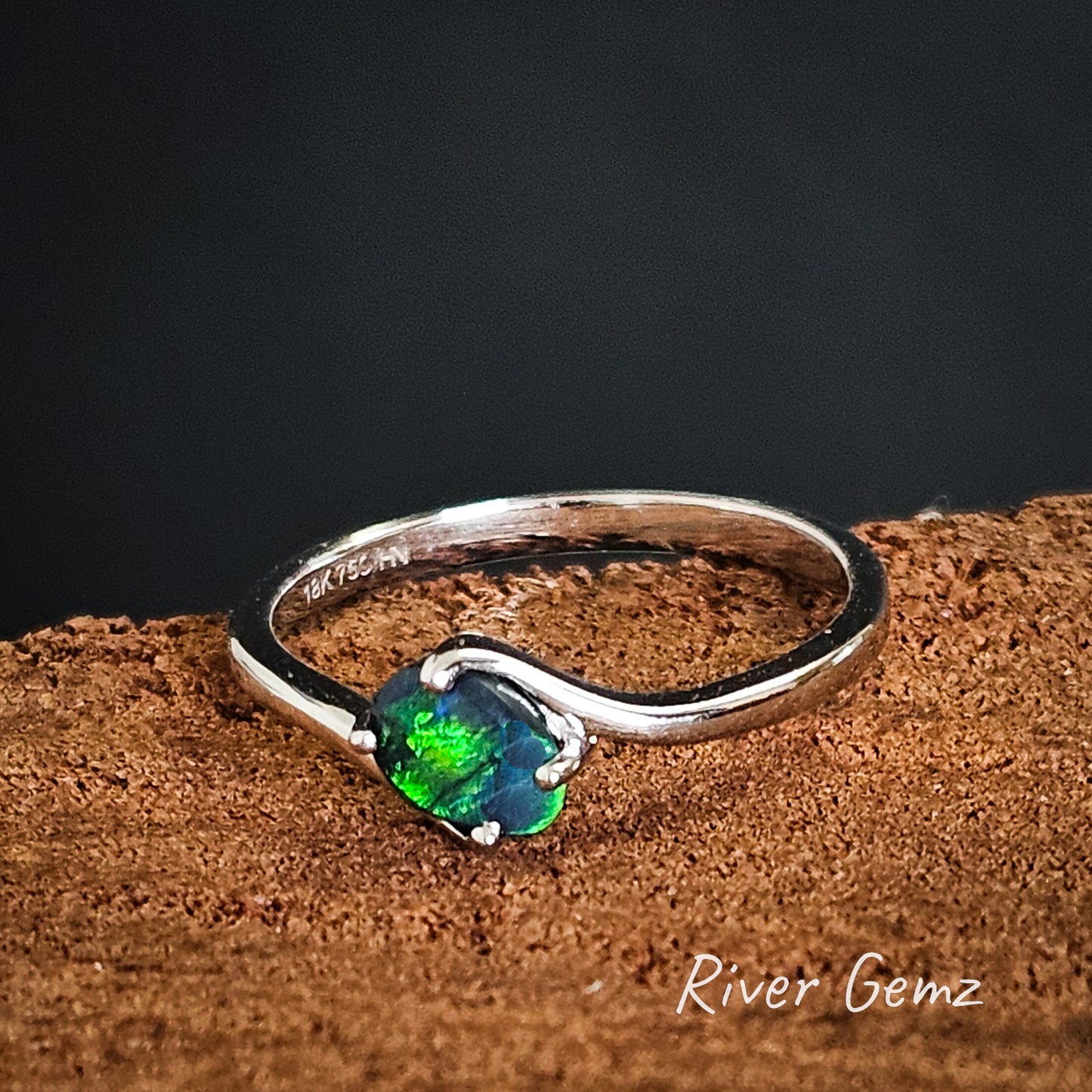 Black opal with dark blue and bright green colours held with 4 claws in white gold ring.