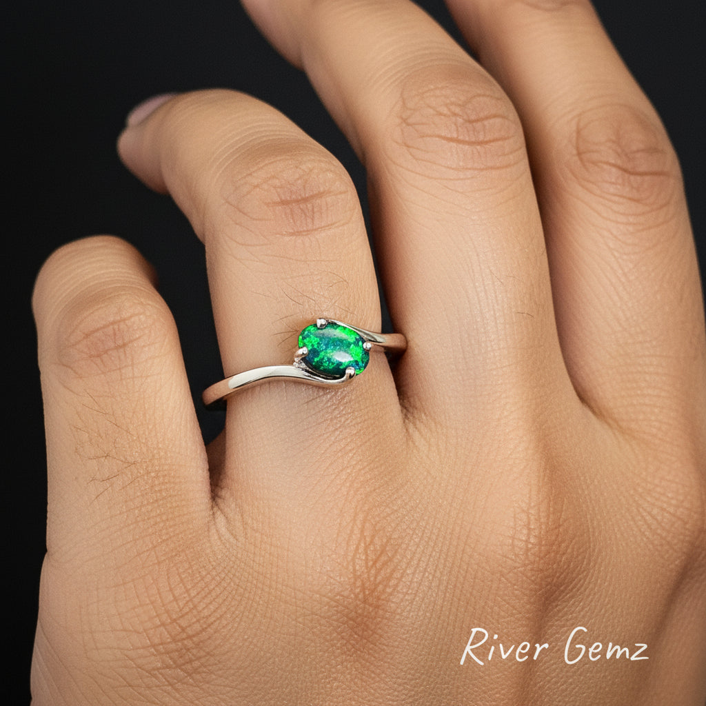 Black opal with dark blue and bright green colours held with 4 claws in white gold ring on the ring finger of the left hand.