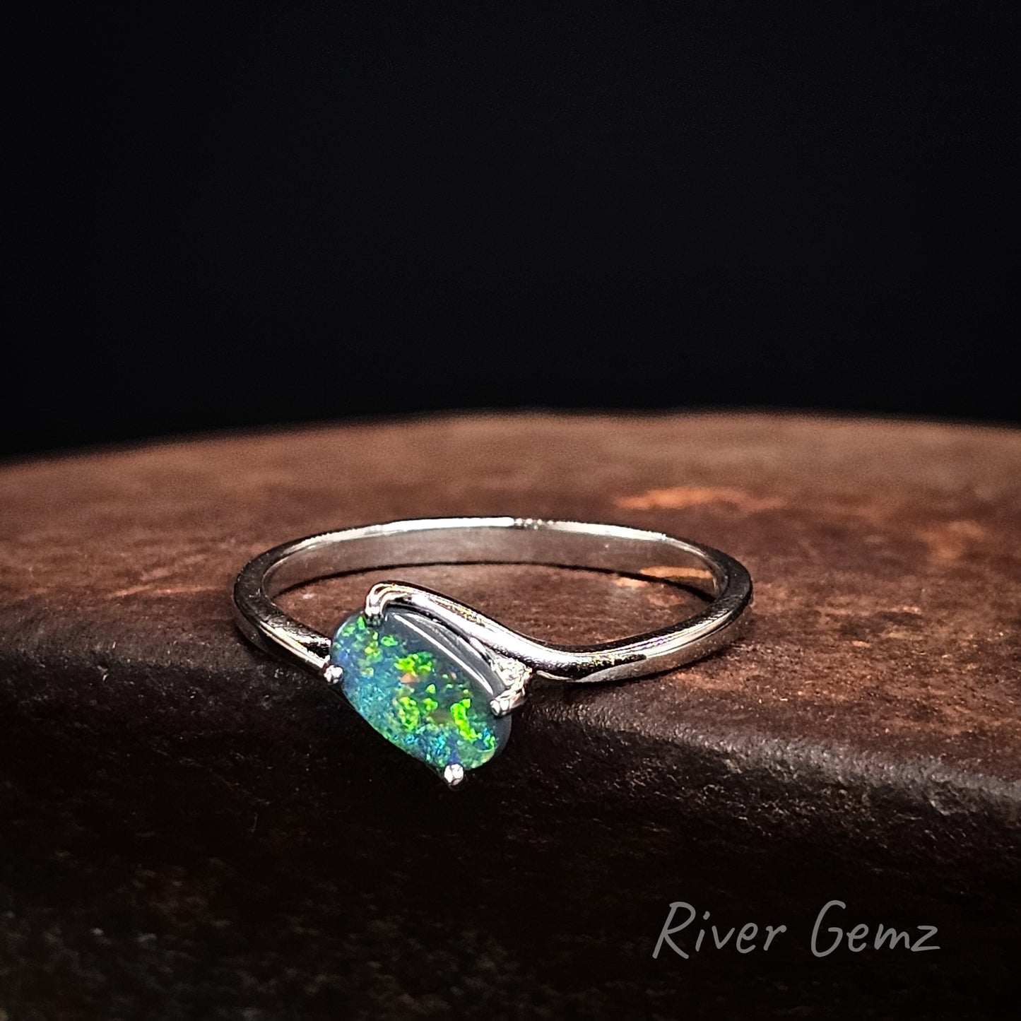 White gold ring with an opal stone on a dark surface, branded 'River Gemz'.