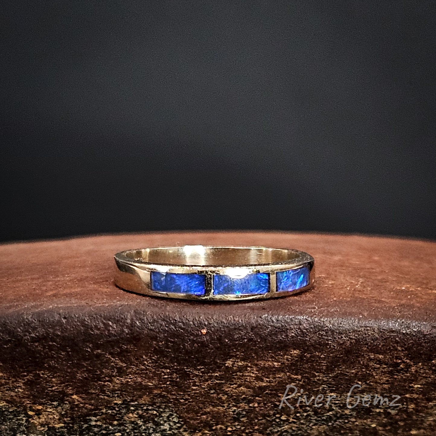 White gold ring with 3 channel set blue stones on a dark surface.
