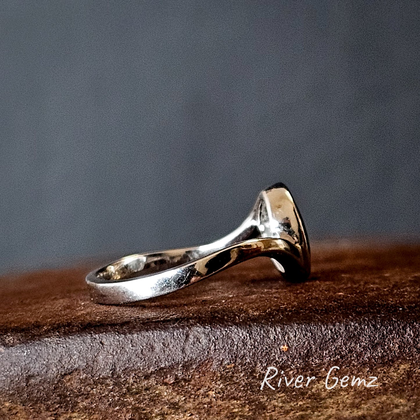 Side view of white gold ring shows the undulating design of the band and the thickness of the besel setting for the opal.