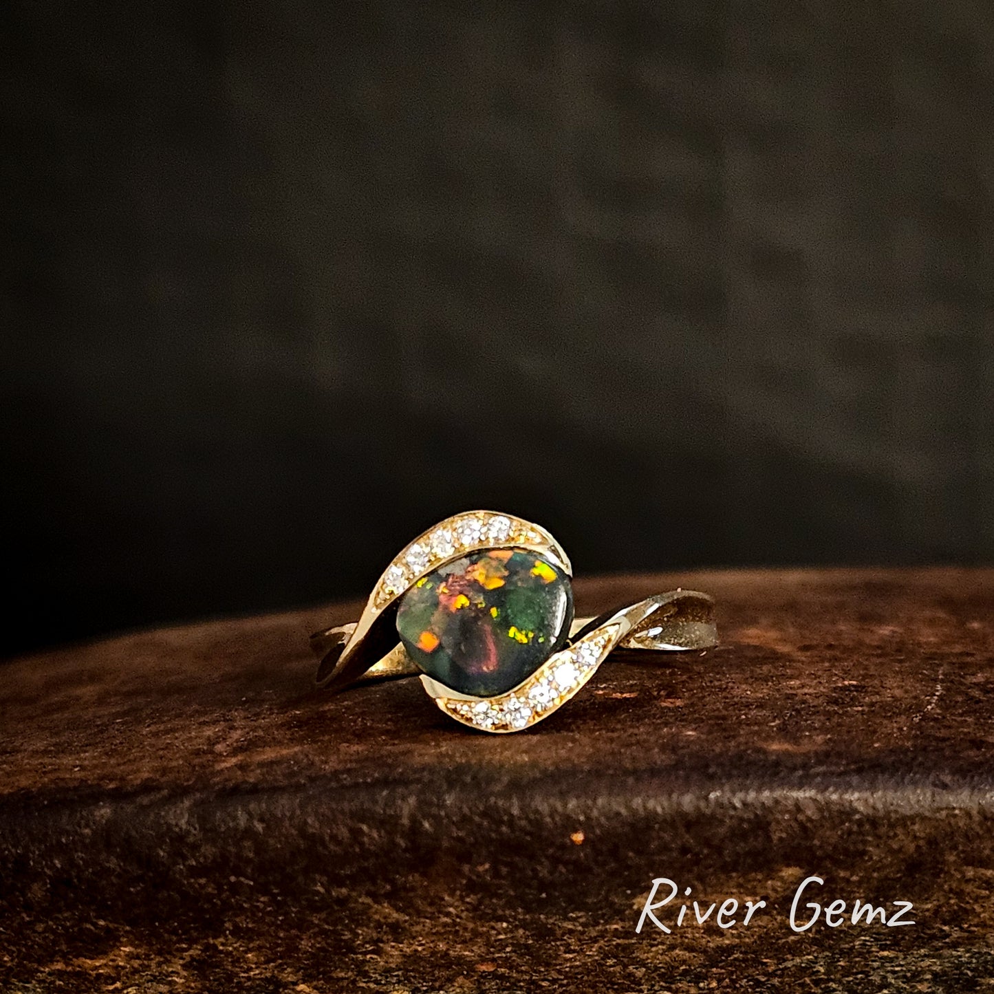 Opal ring with gold band on a dark wooden surface, 'River Gemz' brand visible