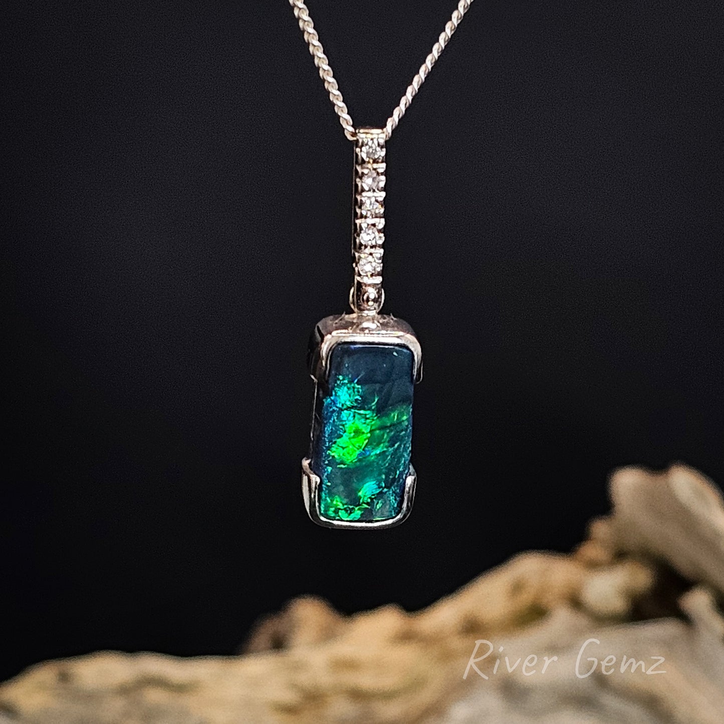 Opal set in a white gold pendant with a silver chain on a dark background, featuring 'River Gemz' branding.