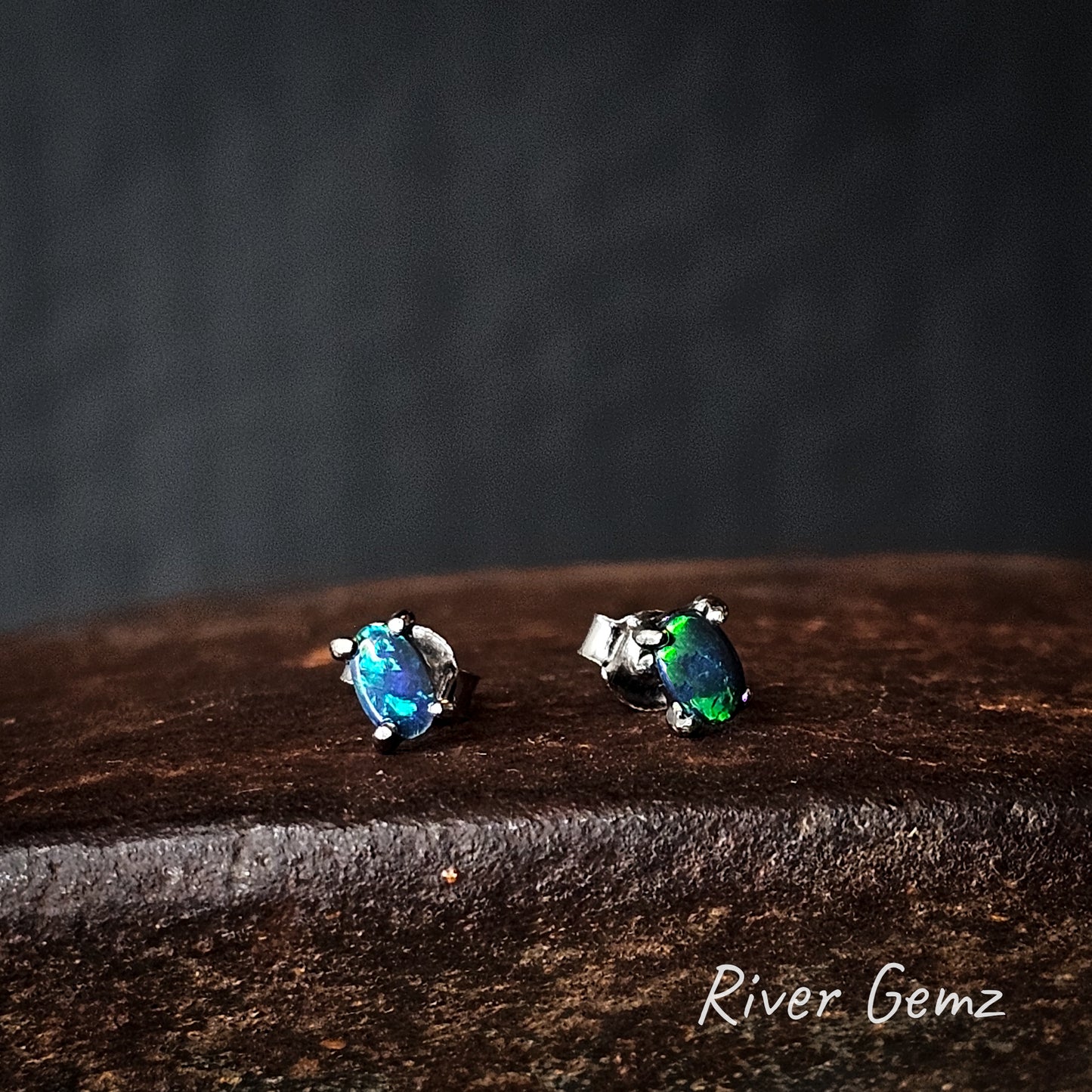 Dark opal claw set in silver studs on a dark surface with 'River Gemz' branding.