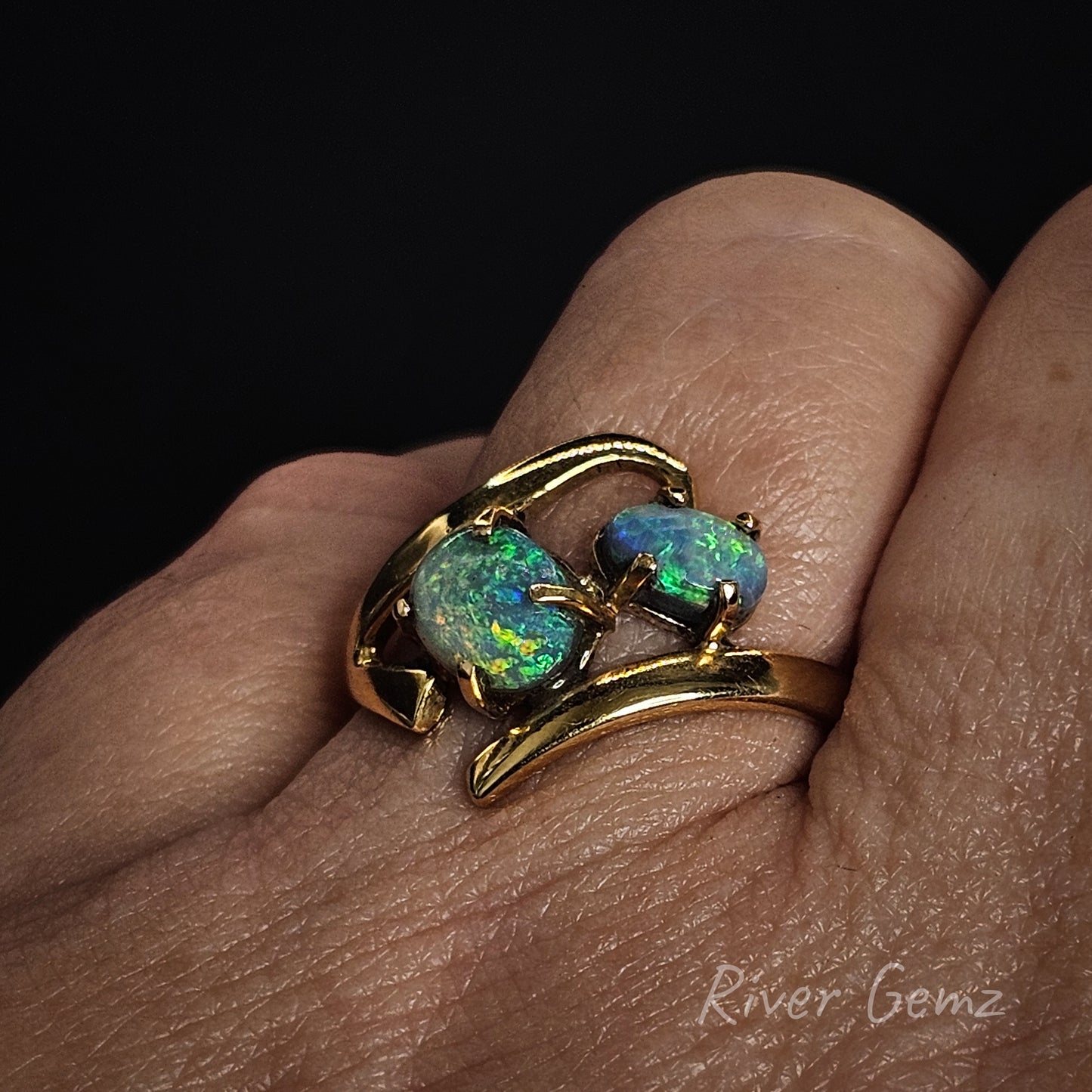 Gold ring with two opal stones on a finger against a dark background