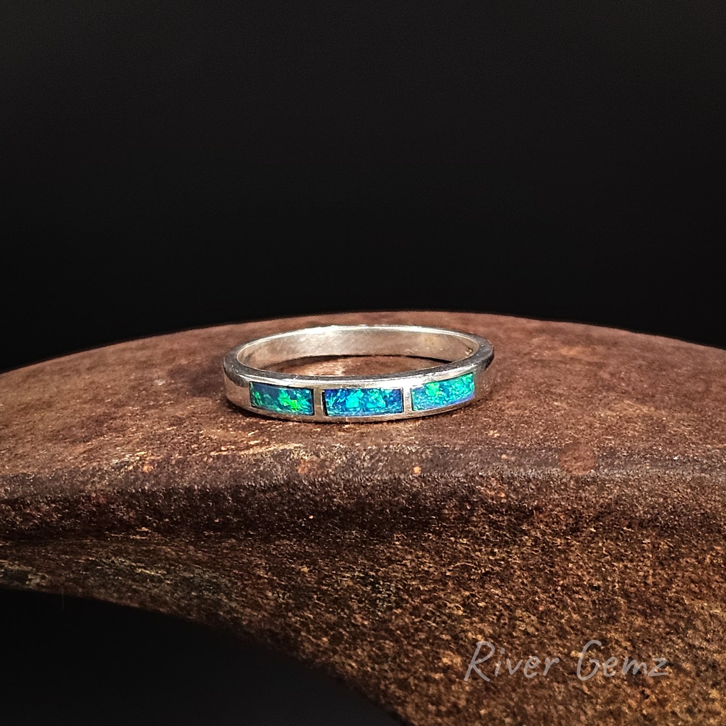 Silver ring with embedded green and blue opal stones on a dark background