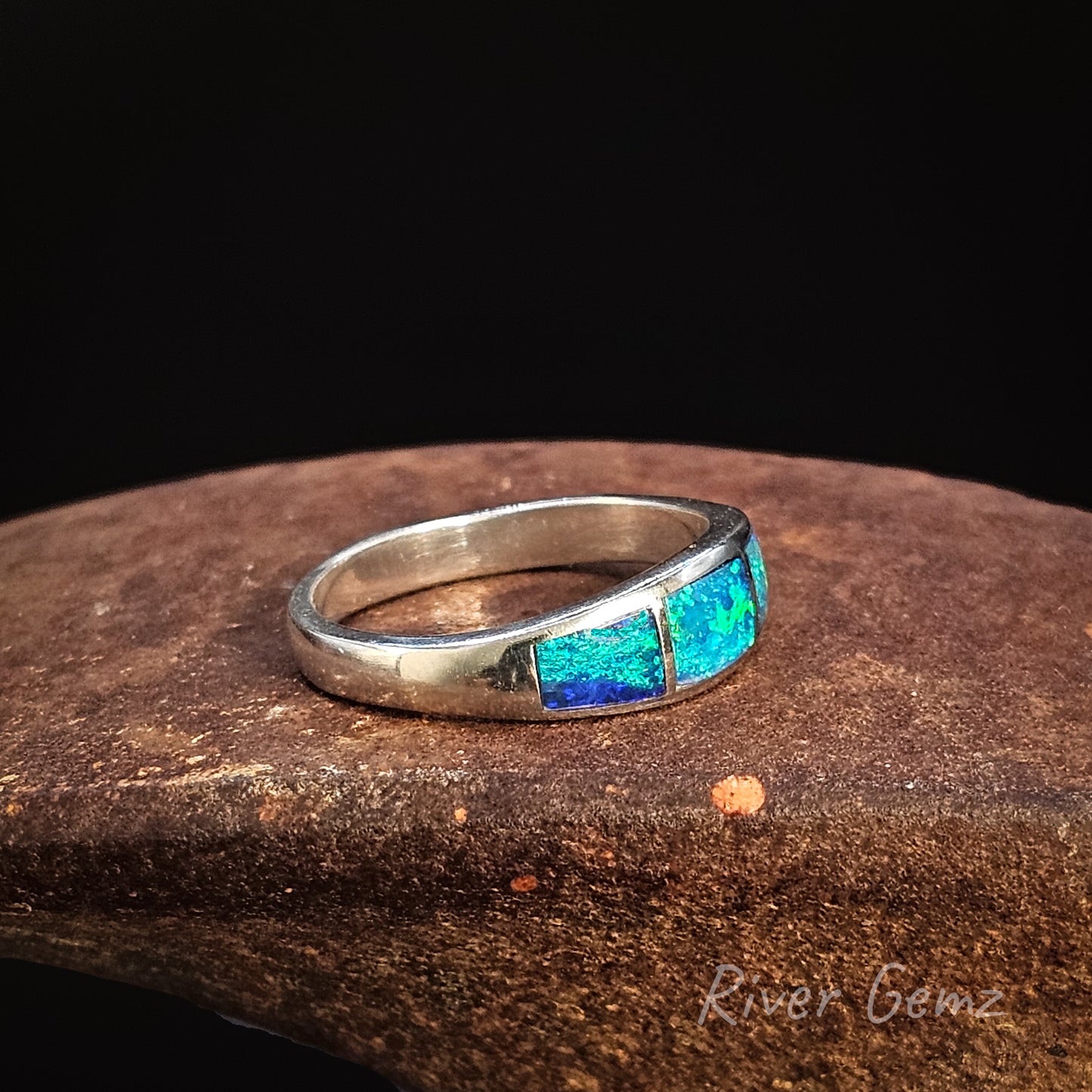 Silver ring with blue and green inlay on a dark surface, branded 'River Gemz'.