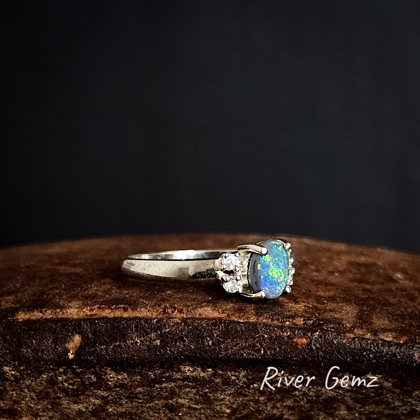 Oval shaped opal set in sterling silver ring on a rusty surface with 'River Gemz' branding.