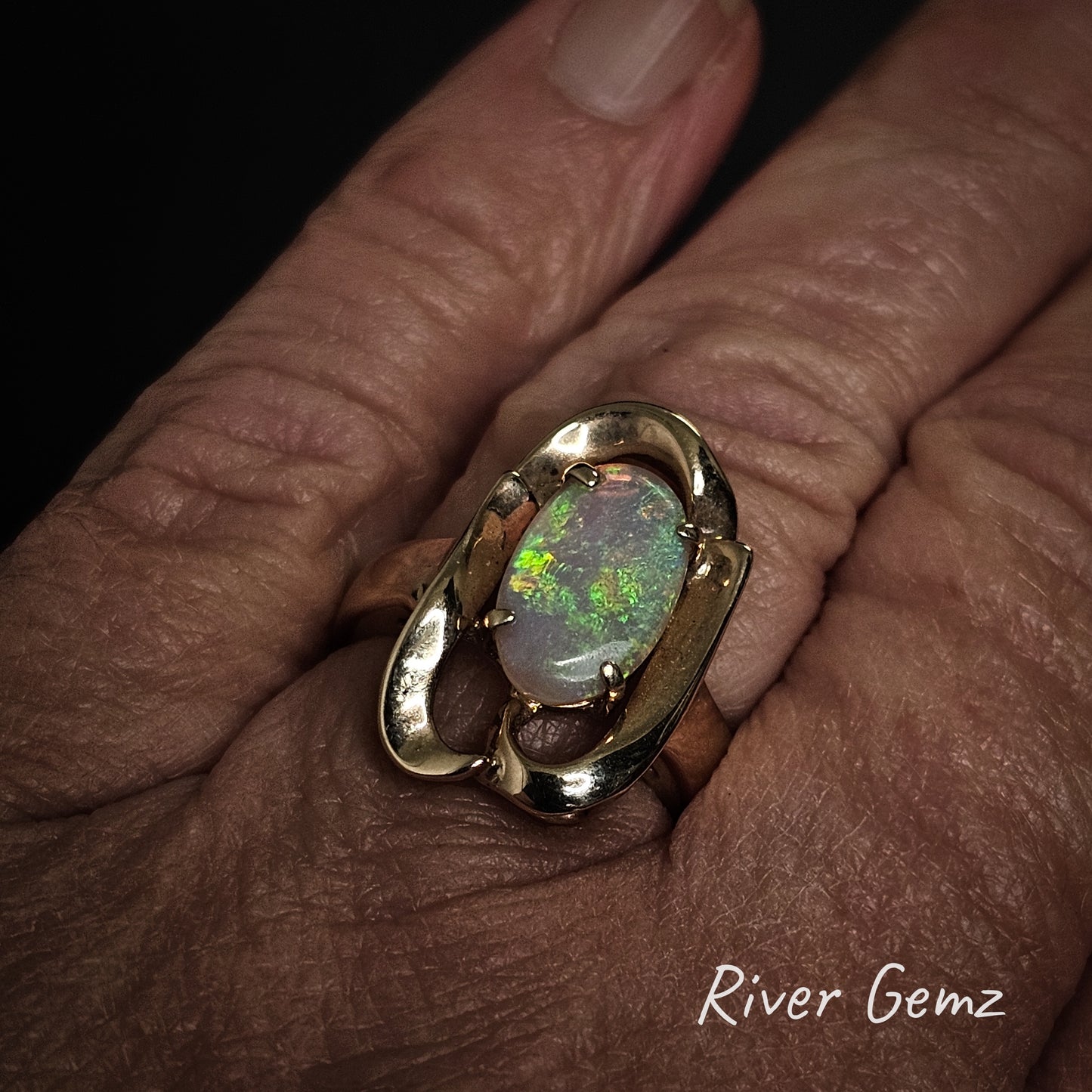 Gold ring with an opal stone on a hand, branded 'River Gemz'.