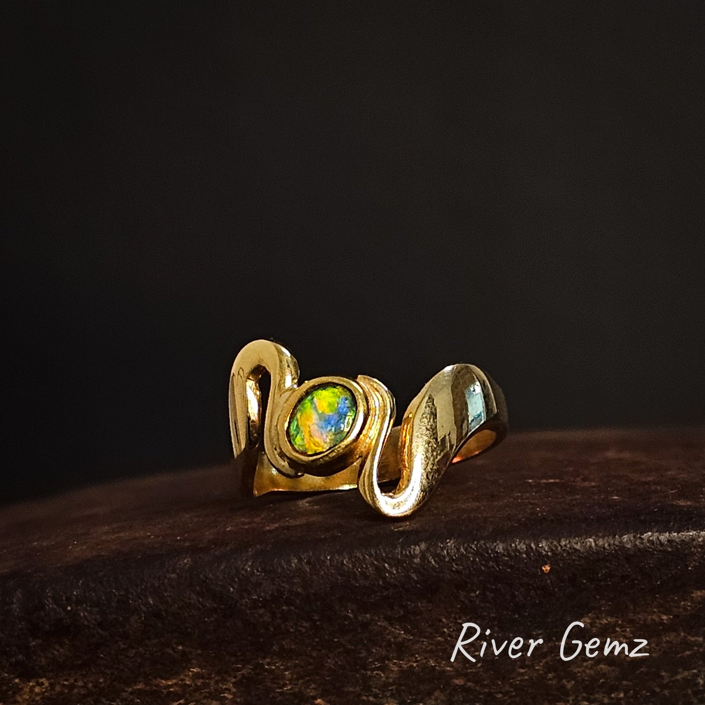 Gold ring with a colorful light opal on a dark background, branded 'River Gemz'.