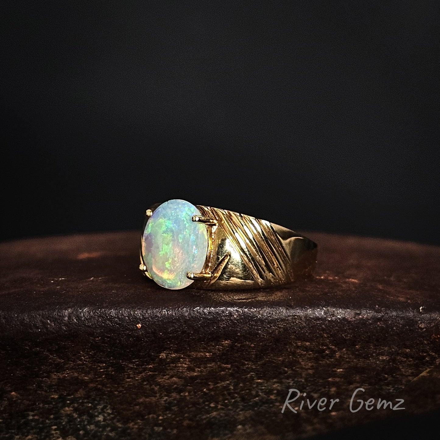 Gold ring with an opal stone on a dark background, featuring 'River Gemz' branding.