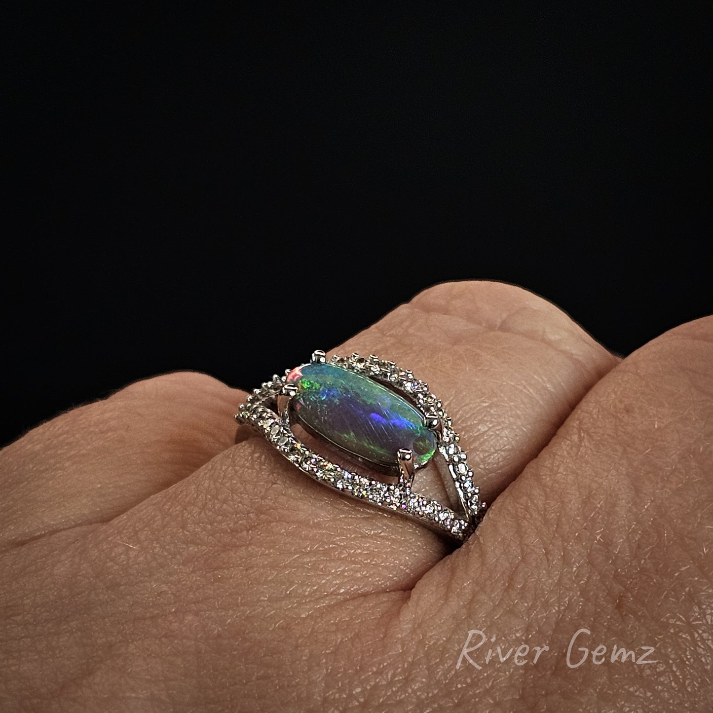 Ring with a colorful gemstone on a finger against a black background
