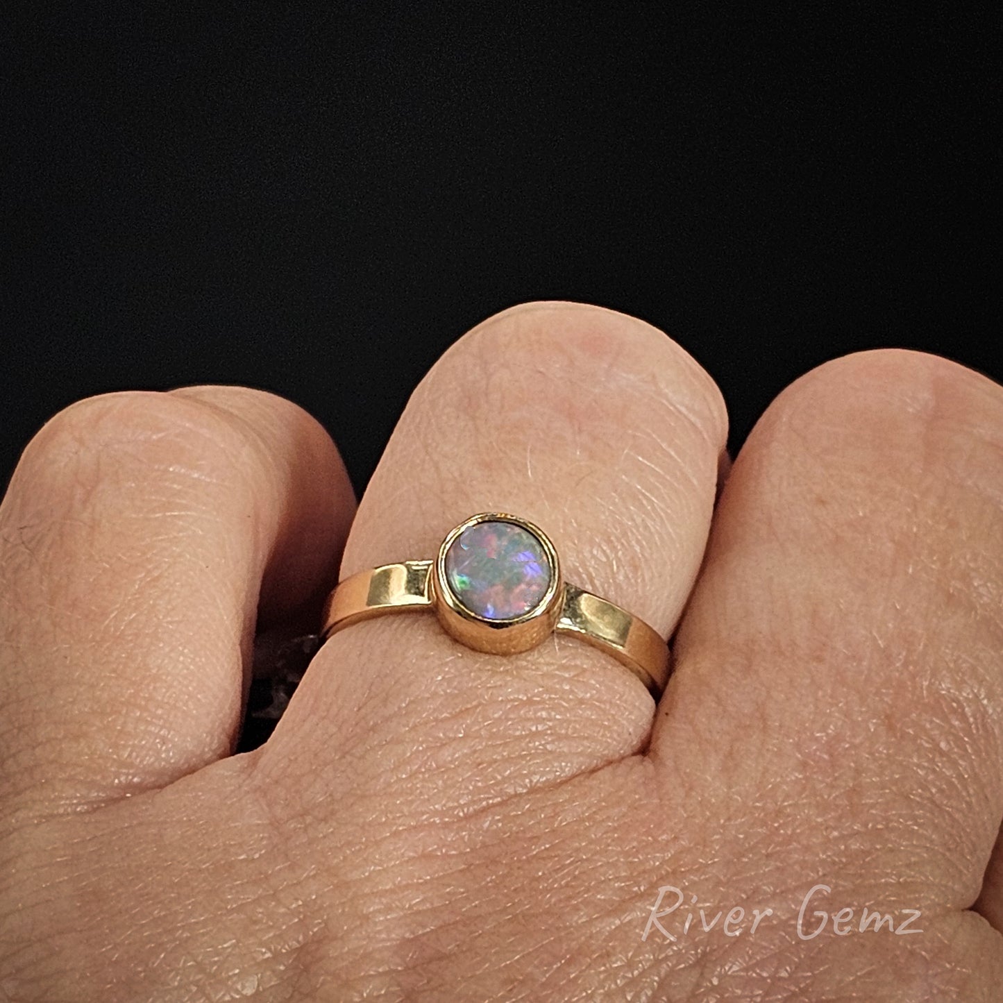 Gold ring with an opal stone on a finger, branded 'River Gemz'.