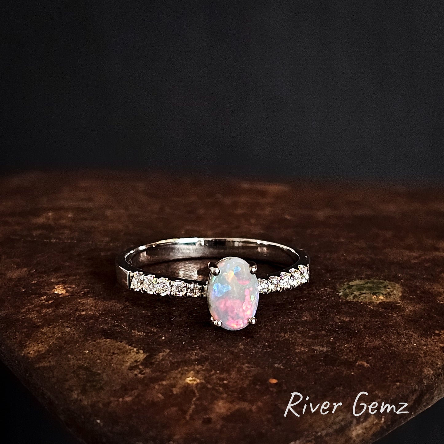 Silver ring with a pink and light green opal and topaz stones on a dark surface, branded 'River Gemz'.
