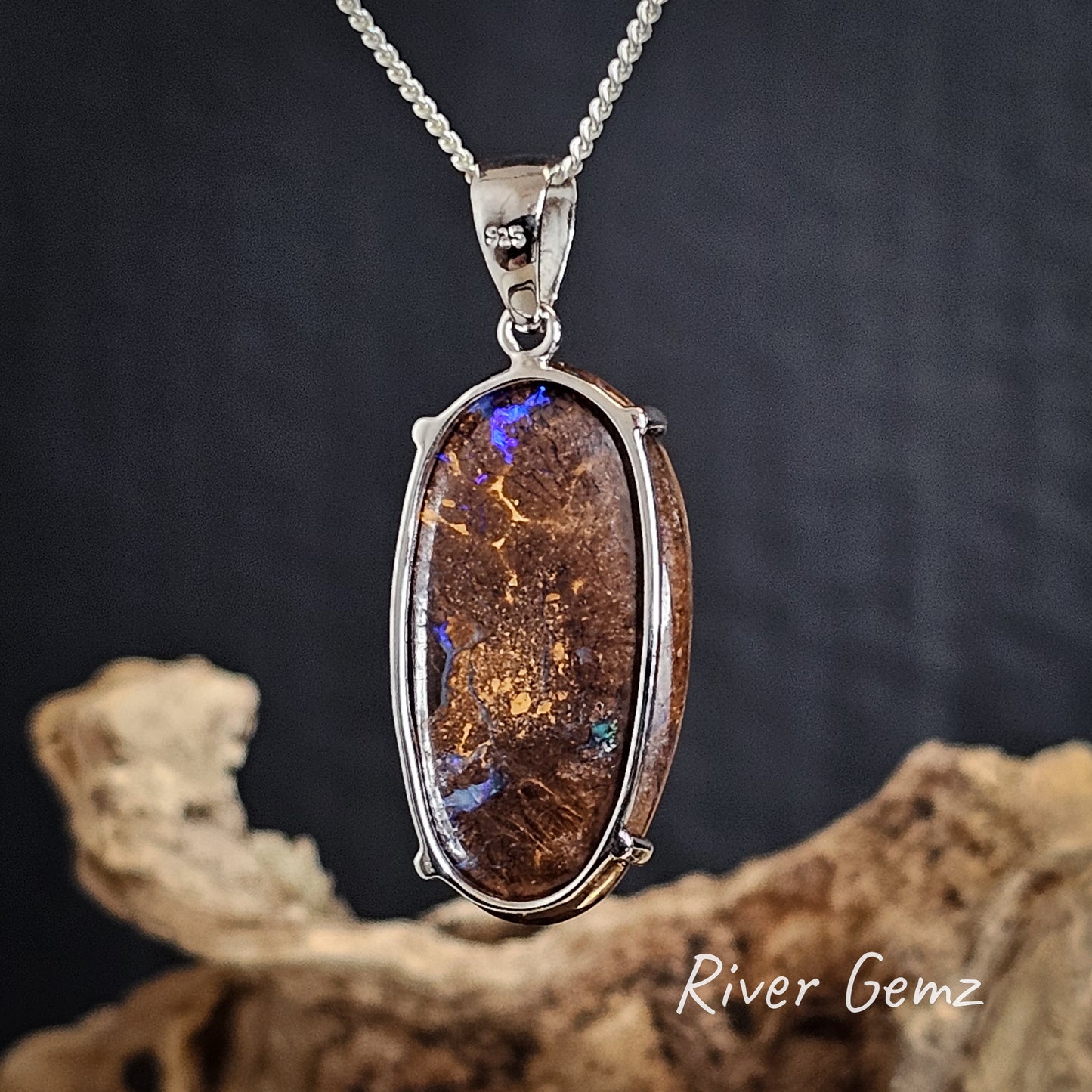 Back of opal pendant in a silver setting on a dark background with 'River Gemz' branding.