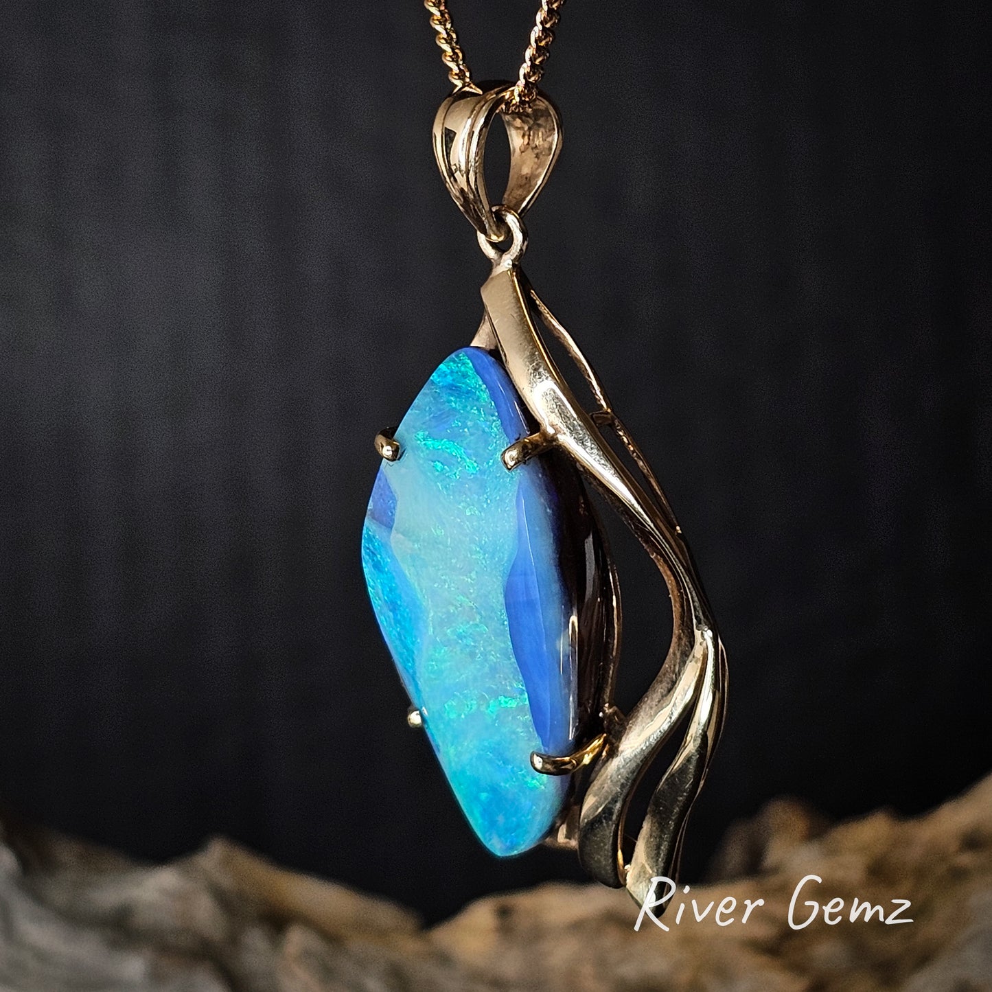Opal pendant with gold setting on a dark background, featuring 'River Gemz' branding.