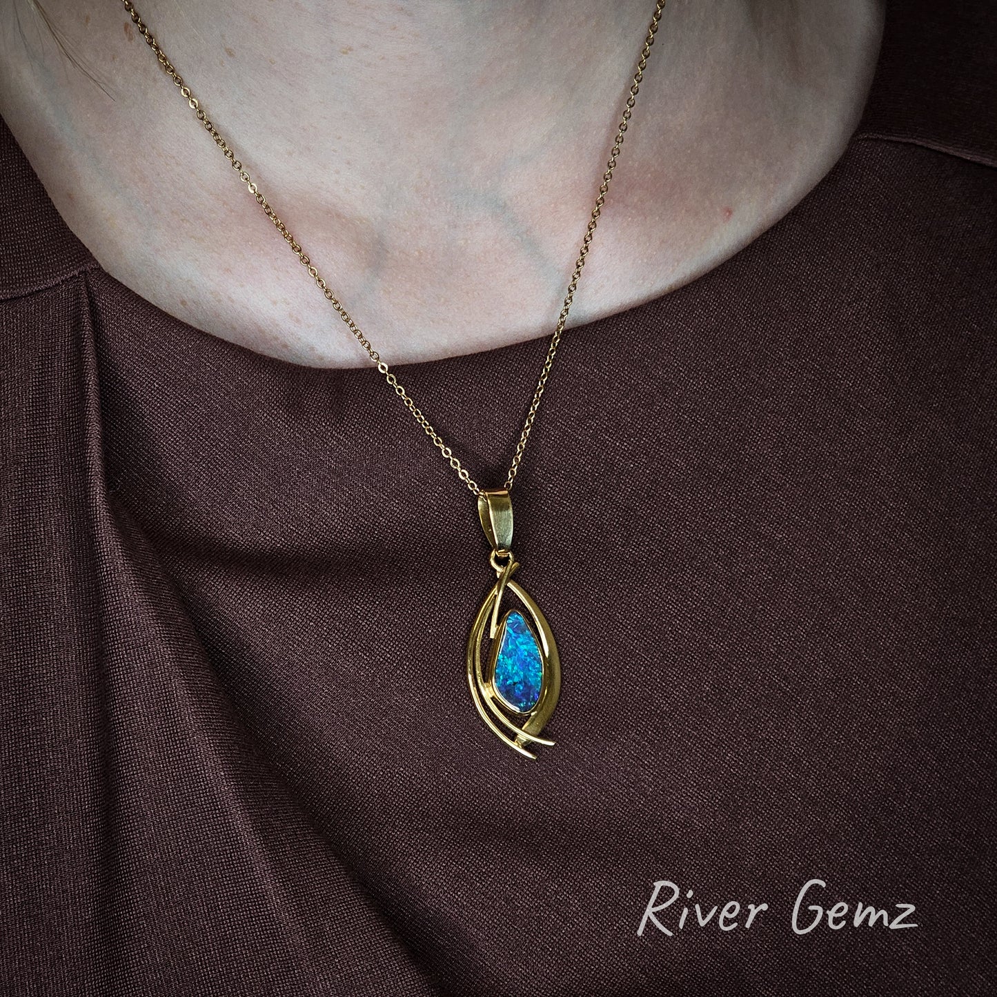 Blue and green opal set in yellow gold pendant worn by person in a dark dress.