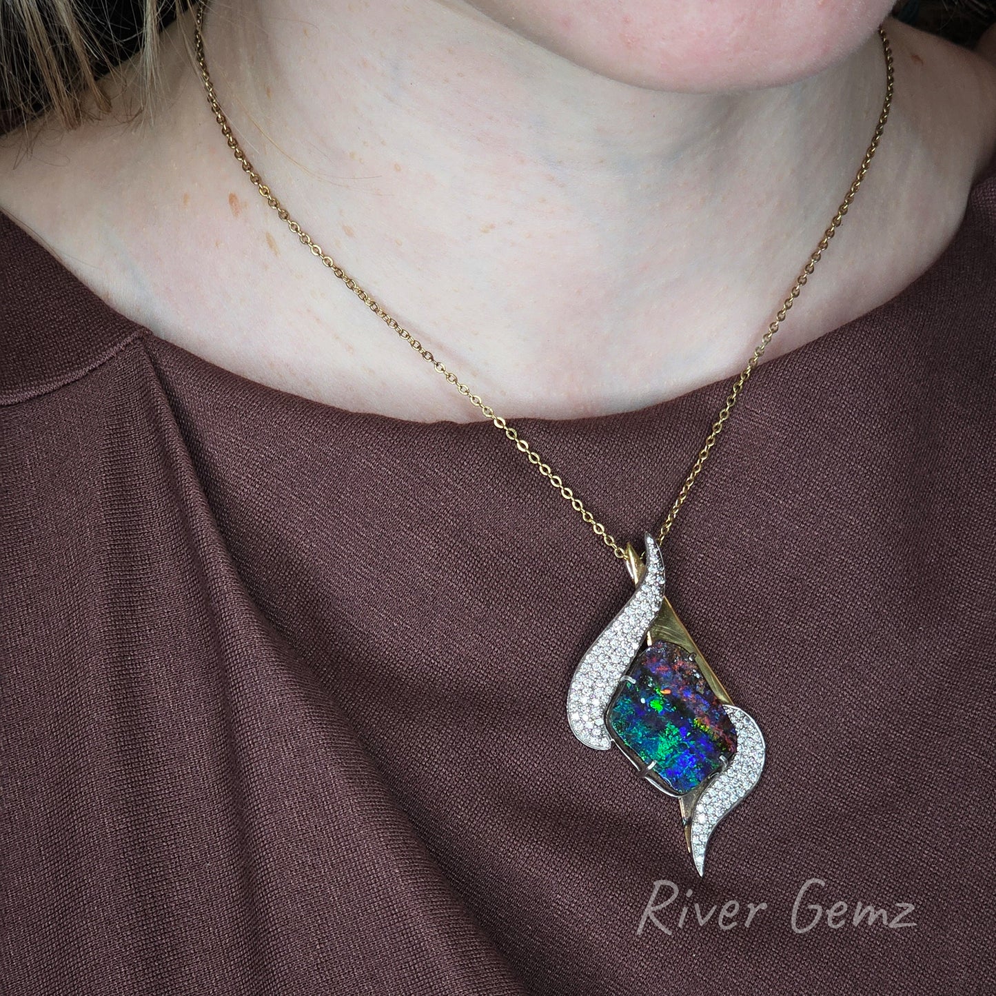Yellow gold necklace with a colourful opal and multiple diamonds on a brown dress, featuring 'River Gemz' branding.