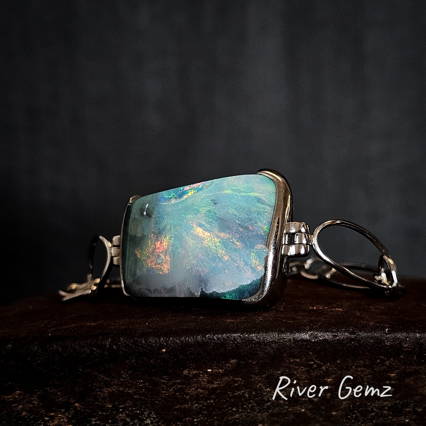 Opal set in sterling silver bracelet on a dark surface, 'River Gemz' branding visible.