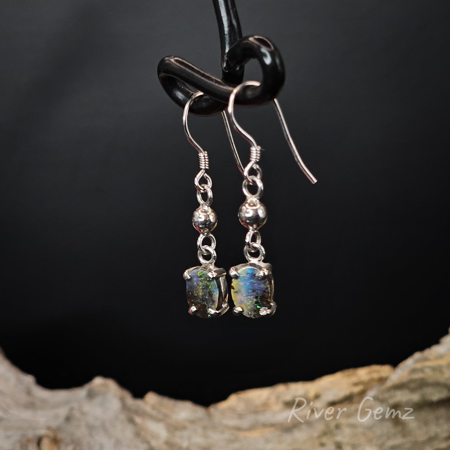 Silver earrings with gemstones hanging on a dark background