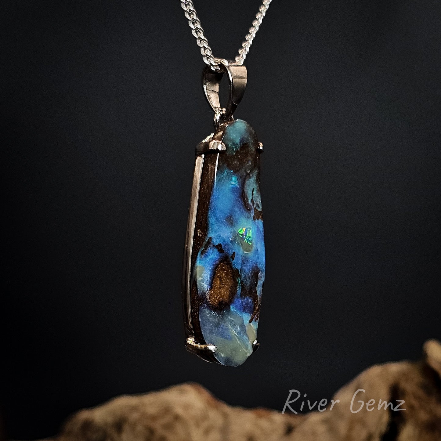 Blue boulder opal claw set in sterling silver pendant on a chain against a dark background