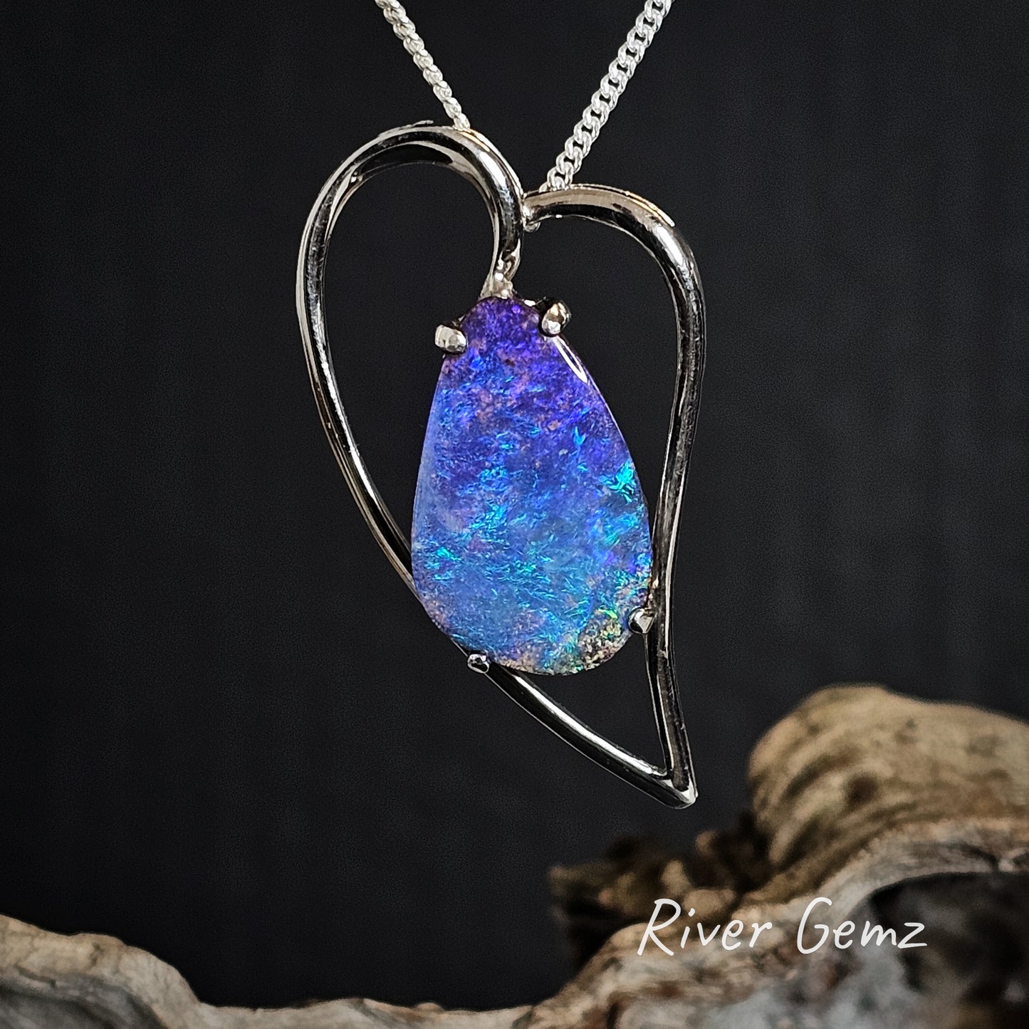 Silver heart-shaped pendant with a blue opal stone on a dark background, branded 'River Gemz'.