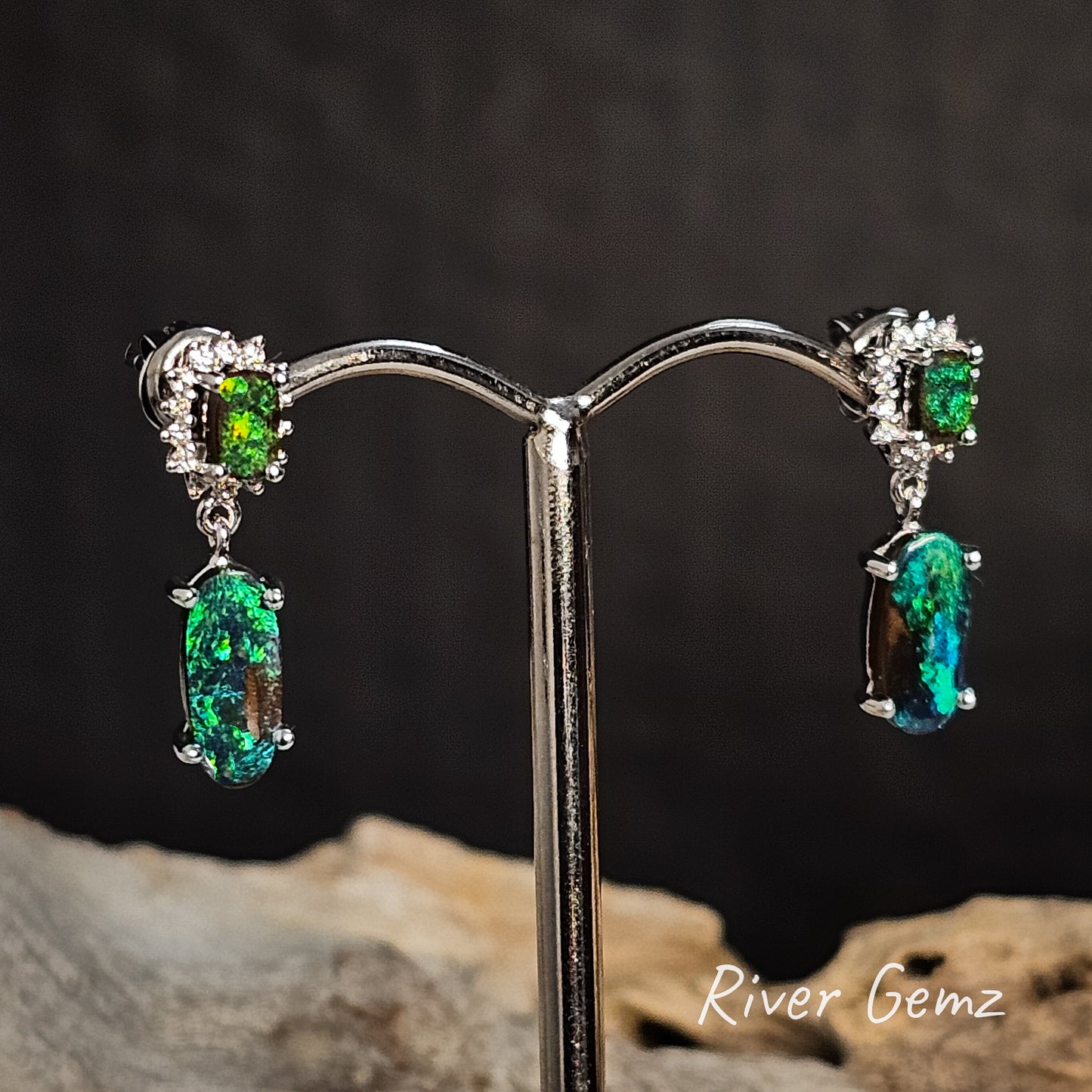 Pair of earrings with green gemstones on a stand against a dark background'