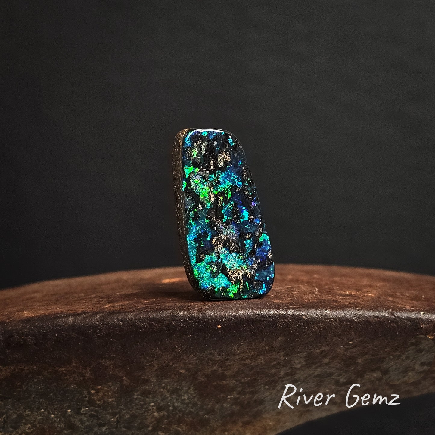 Multicolored gemstone on a cast iron shoe anvil with 'River Gemz' branding.