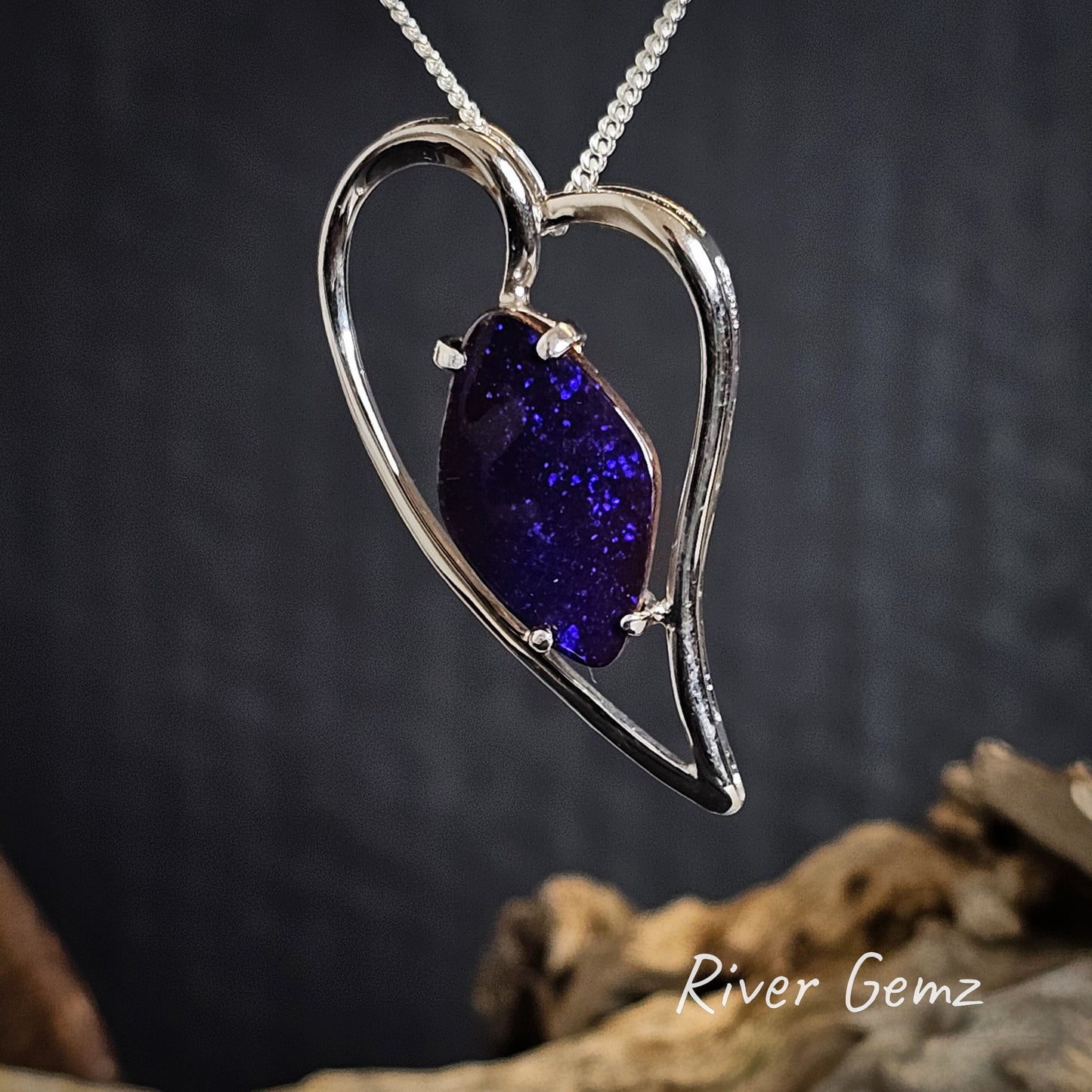 Heart-shaped silver pendant with a purple gemstone on a dark background, featuring 'River Gemz' branding.