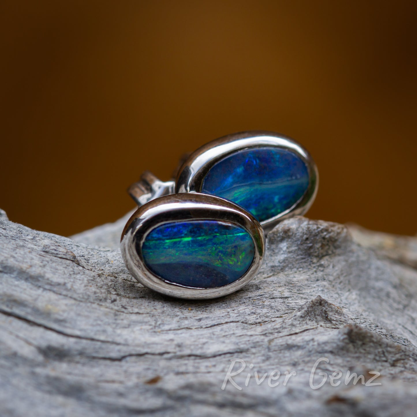 Free form cut opals in an oval shape sit securely in these besel set stud earrings. Each opal has divisions of colours running their length.