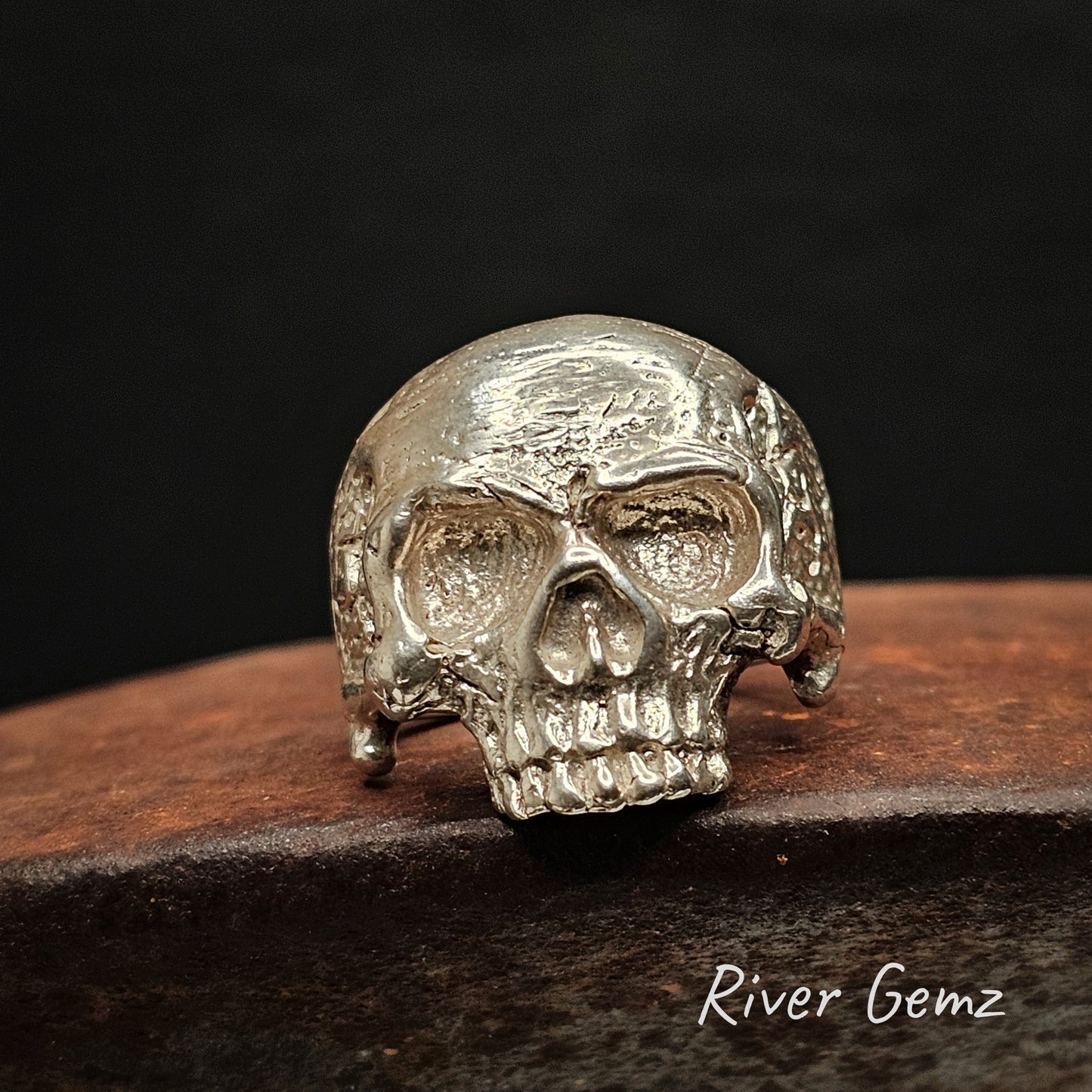 Silver skull-shaped ring on a dark background with 'River Gemz' branding.