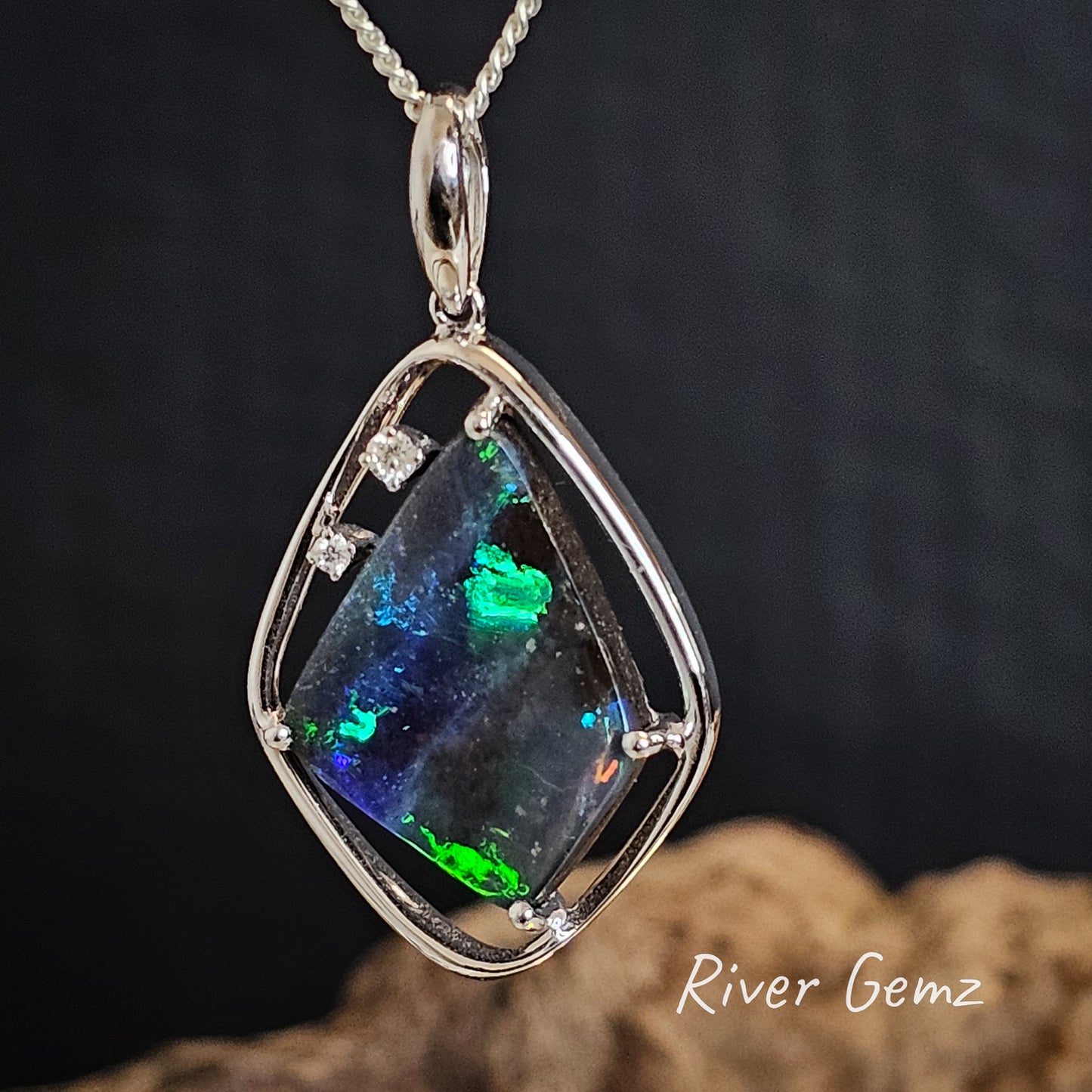 Large spheres of green in the four-sided black boulder opal set in a rounded-corner diamond shaped white gold pendant.