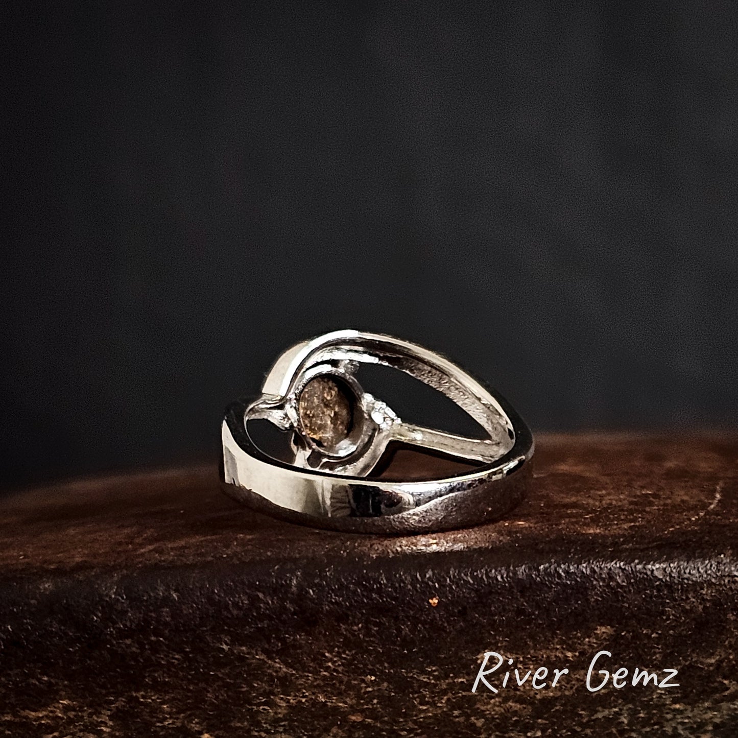 Back of silver ring shows the ironstone matrix of the boulder opal on a rust coloured surface, branded 'River Gemz'.