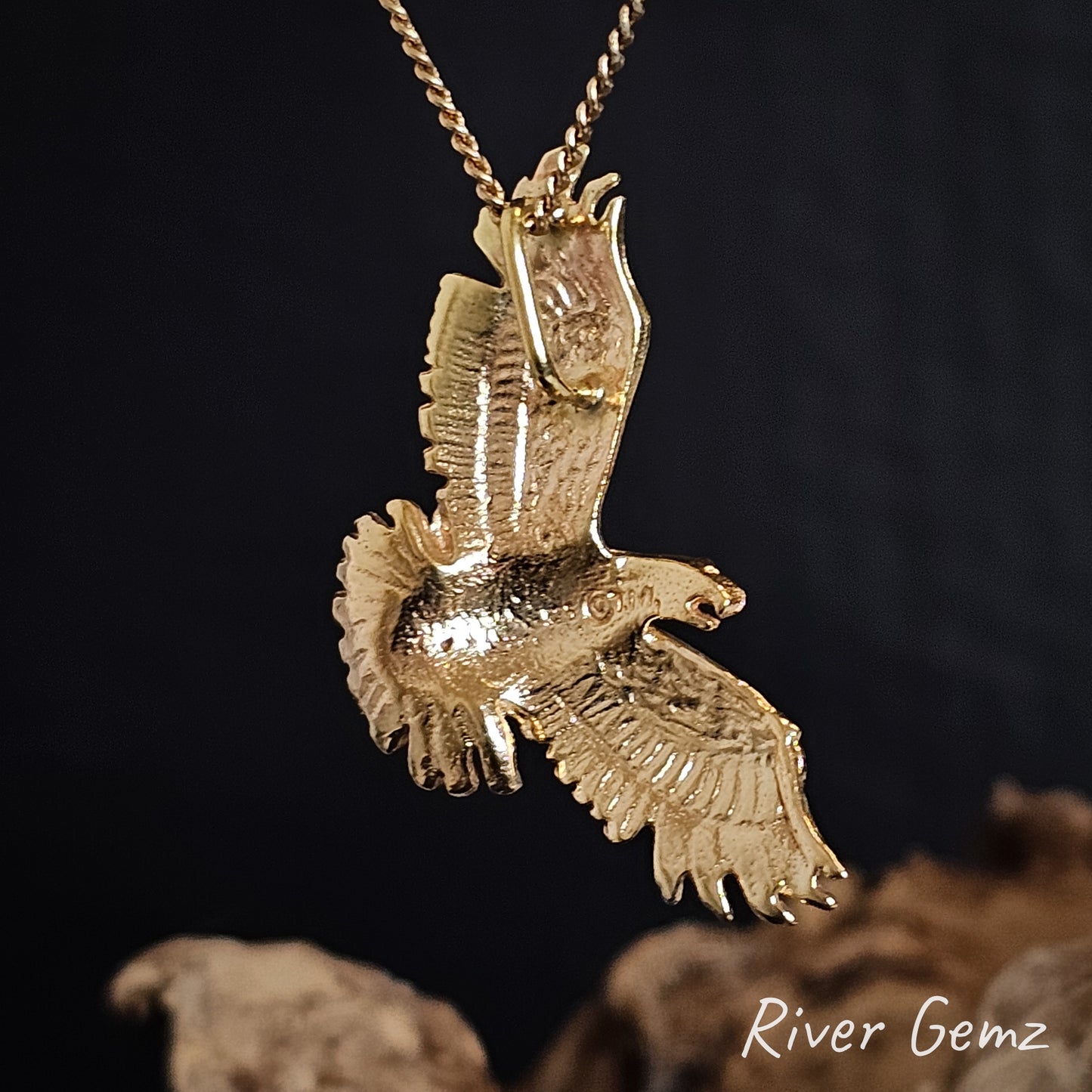 Back of gold eagle pendant on a chain against a dark background with 'River Gemz' branding.