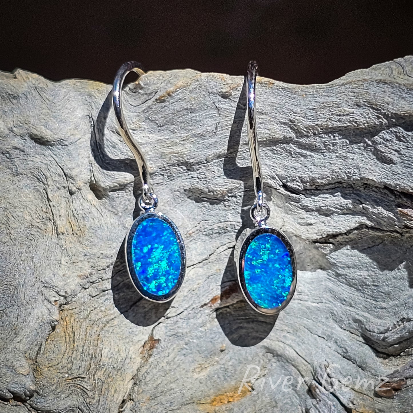 Oval shaped cabochon cut blue green opals besel set. Hooks have an eyelet connection to the dangly opal which will swivel.