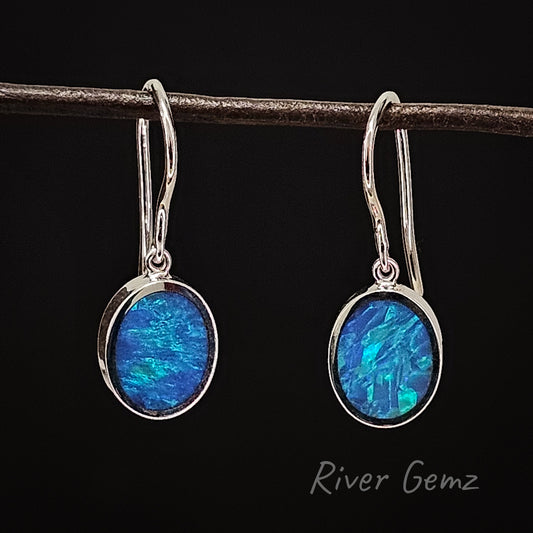 Two blue & green coloured oval shaped opals besel set in white gold hook earrings. The back drop of the photo is black.