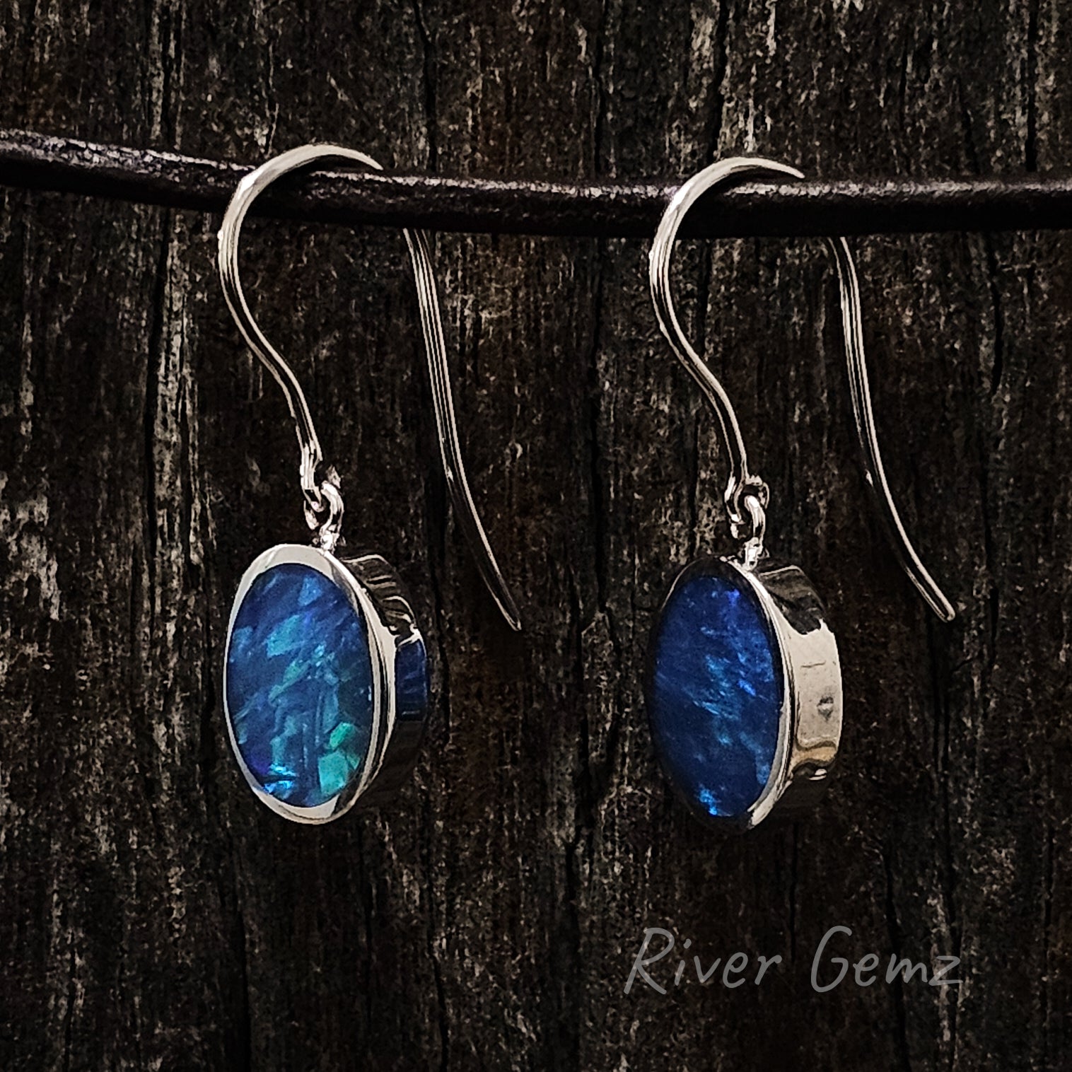 A slightly side on view of the earrings shows the long length of the hooks and the depth of the besel set solid opals.